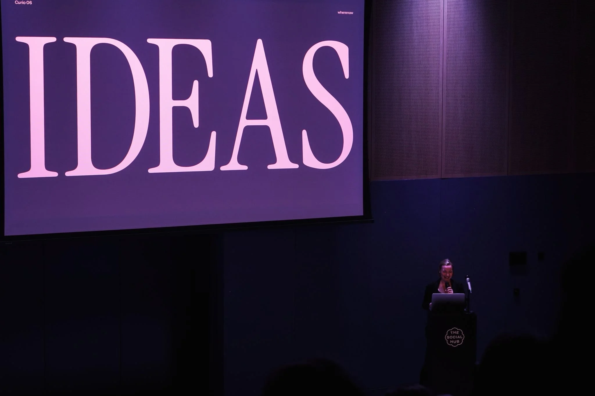 Creative director, Kirsten Murray, speaking on stage at the Curio event. The screen behind her has the word 'Ideas' in large type on it.