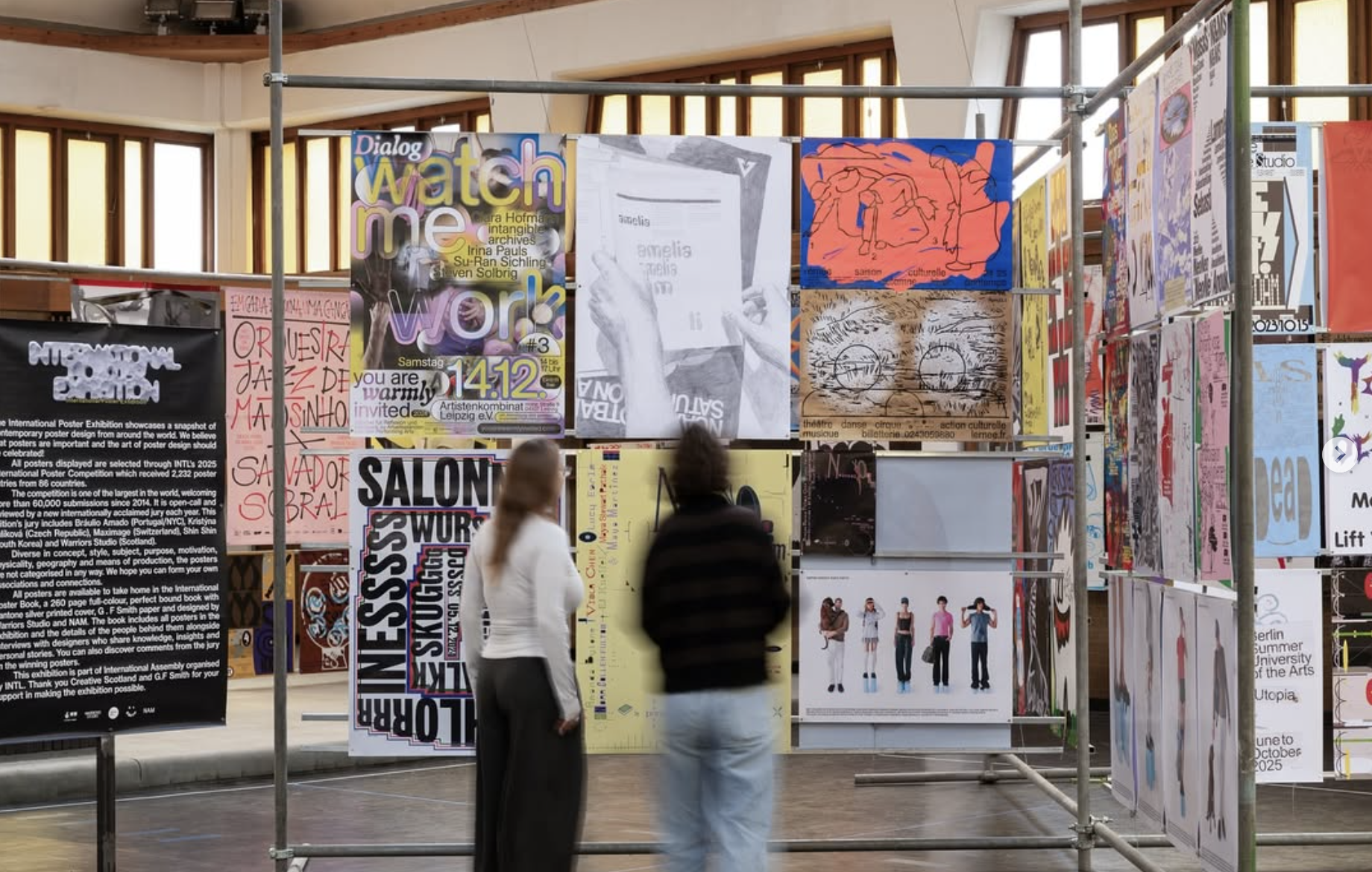 Two people are looking at a series of poster designs exhibited at the INTL poster exhibition in Glasogw.