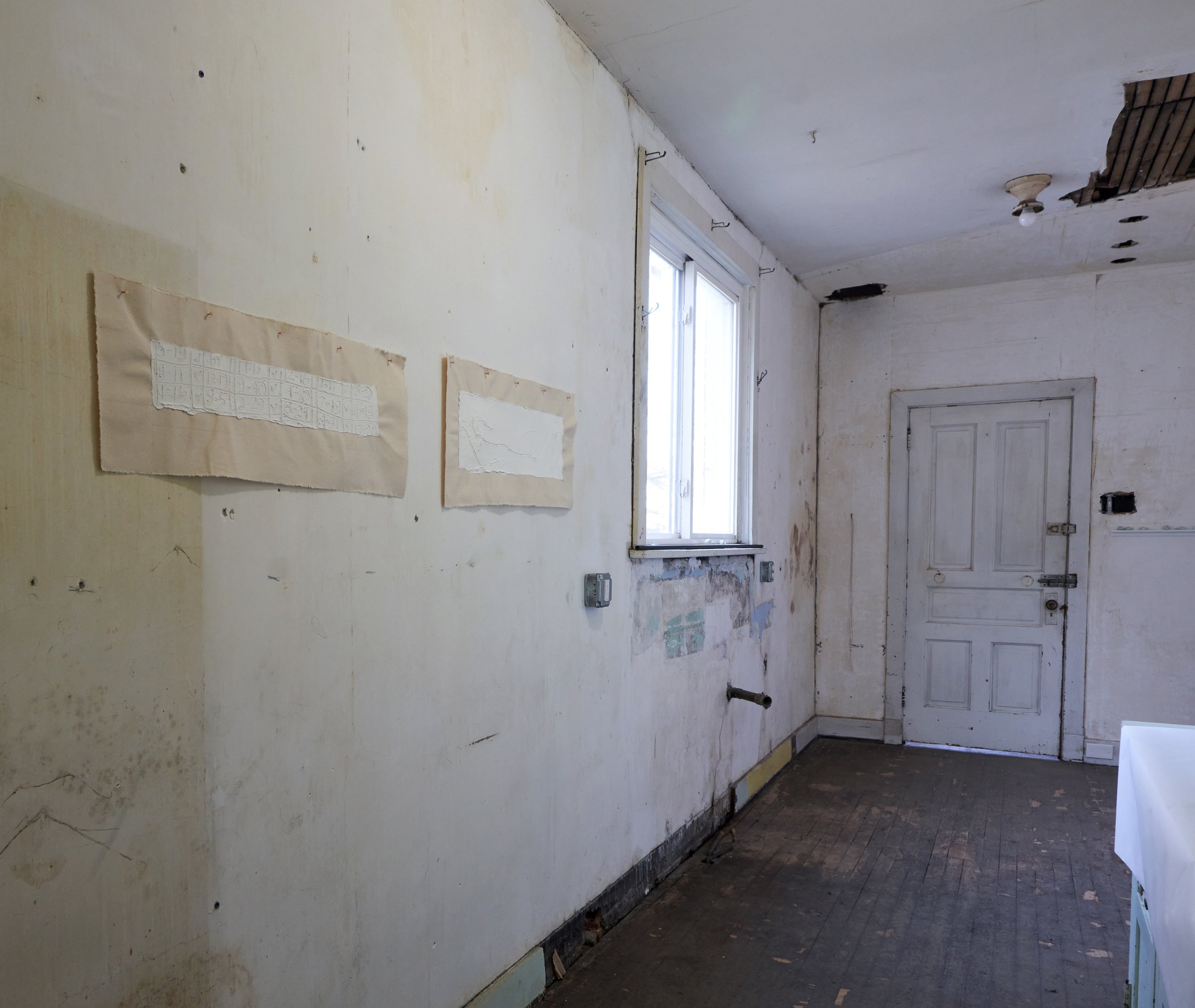  View into former kitchen at blankspace exhibition space.    Response to “Do they even make a 40-person euchre rotation chart?” . Lime plaster on canvas. Canvas: 12 x 32 inches, plaster: 4 x 24 inches.     Response to “I imagine he took the train .” 