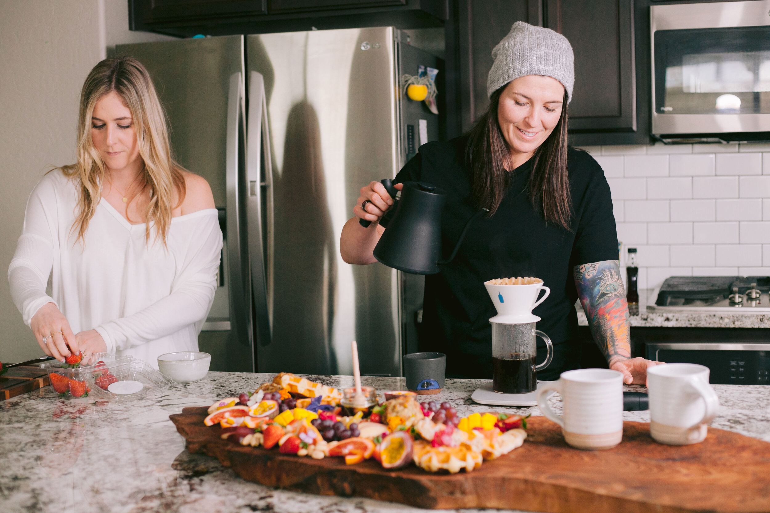 Two women make breakfast in kitchen with coffee and fruit.