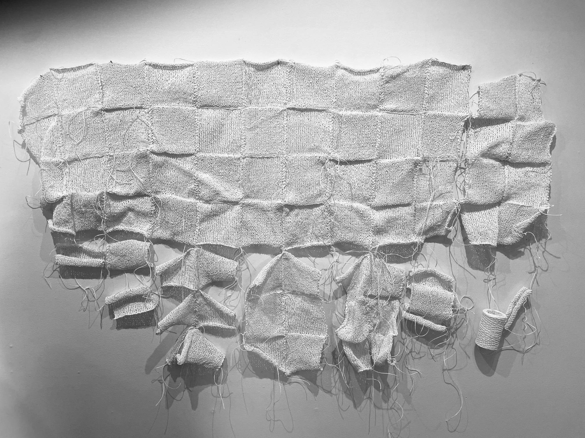 white handknitted squares sewn together making a large rectangle