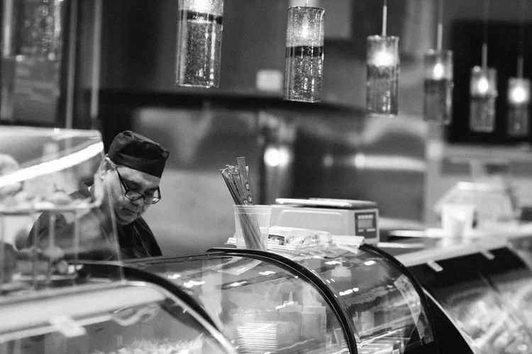 Aroma Market employee wearing chef hat and glasses working at the deli counter.webp