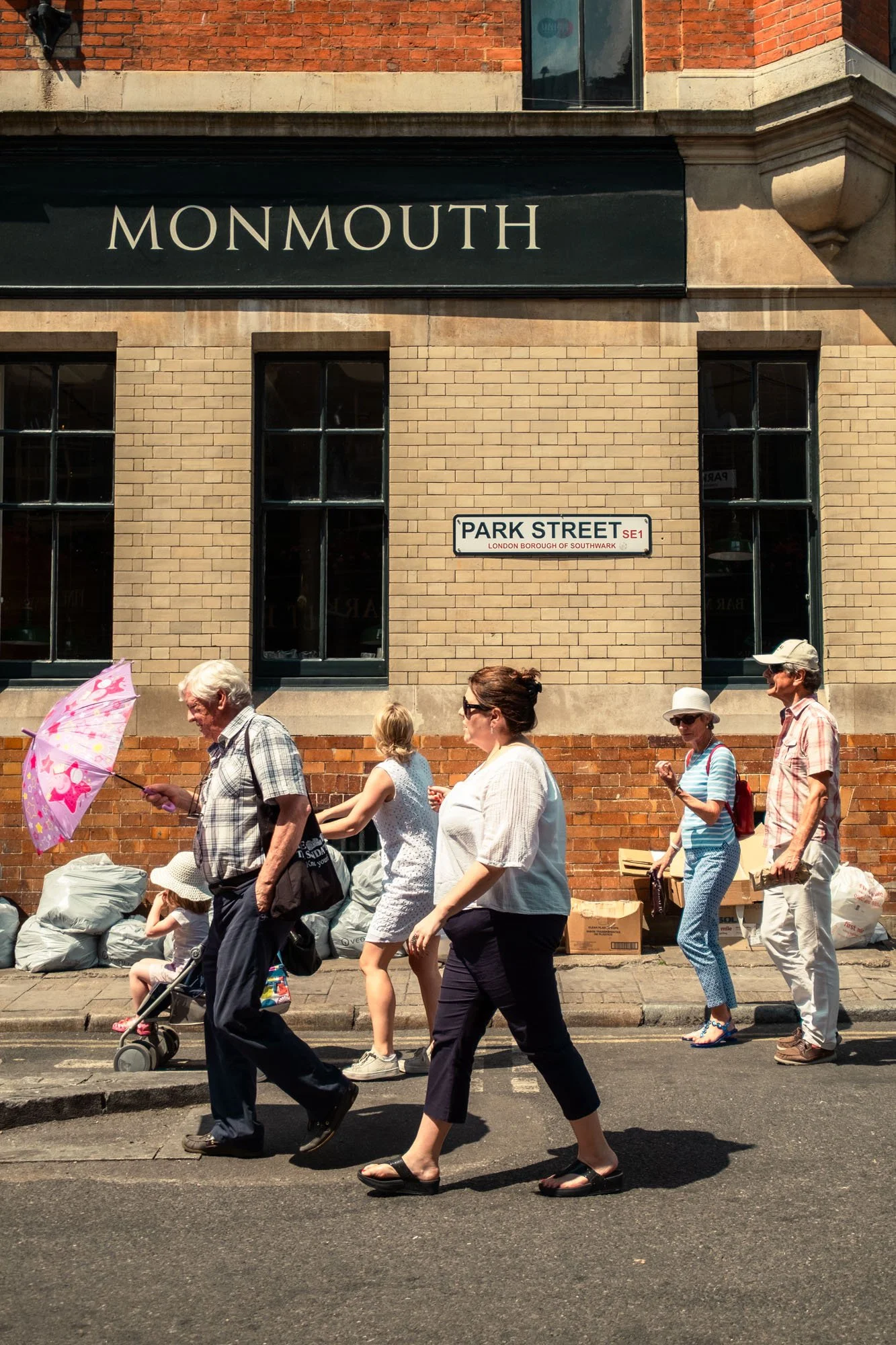 People walking on a city street in front of a brick building with street signs for Monmouth and Park Street in Southwark, London.