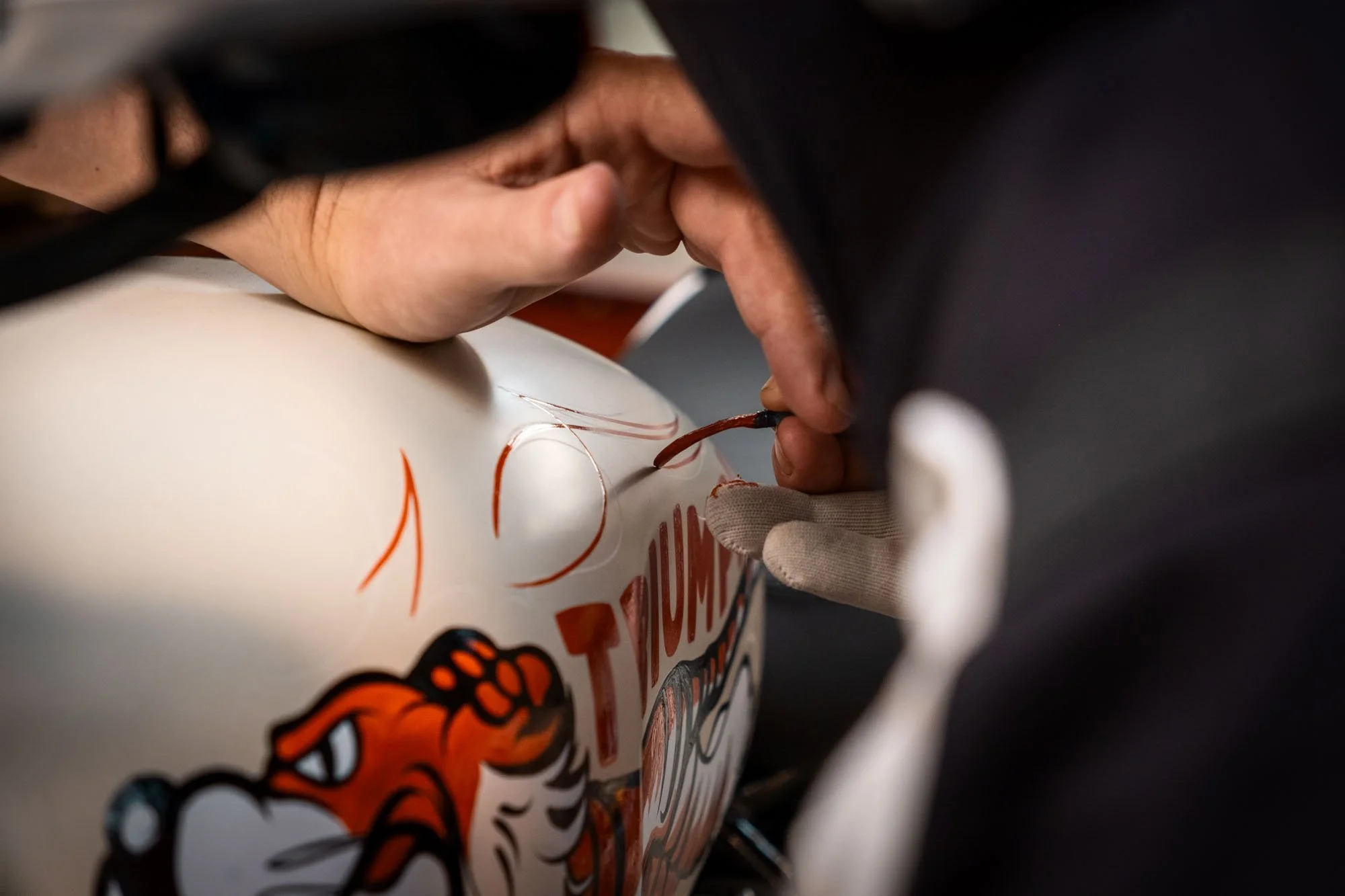 A person signing a white soccer ball with a marker, wearing a black jacket and a white glove on one hand.