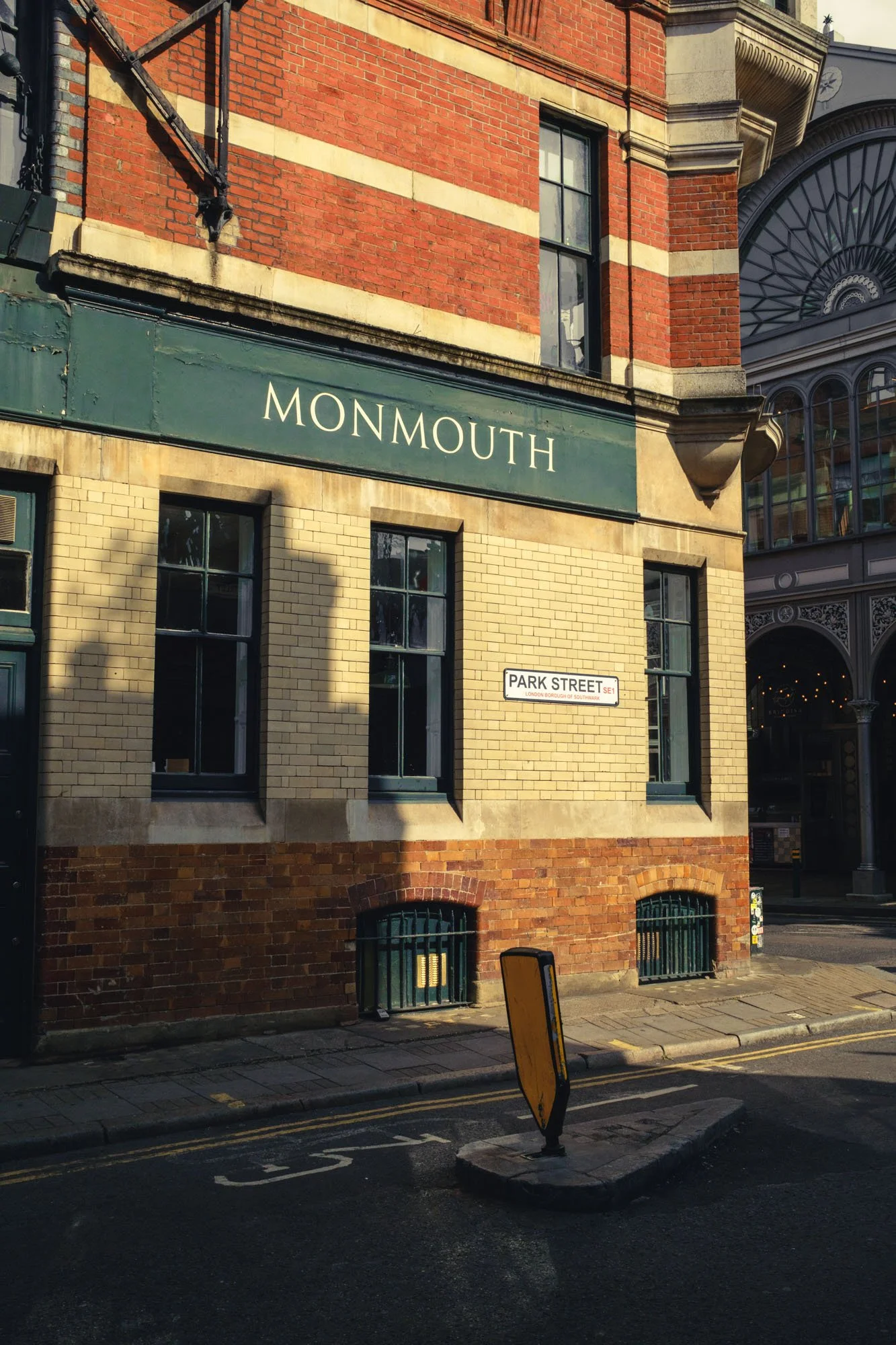 Corner building with a green sign saying 'Monmouth' on a brick storefront, beneath that are three windows and below is a street sign reading 'Park Street', with a yellow traffic barrier in the street.