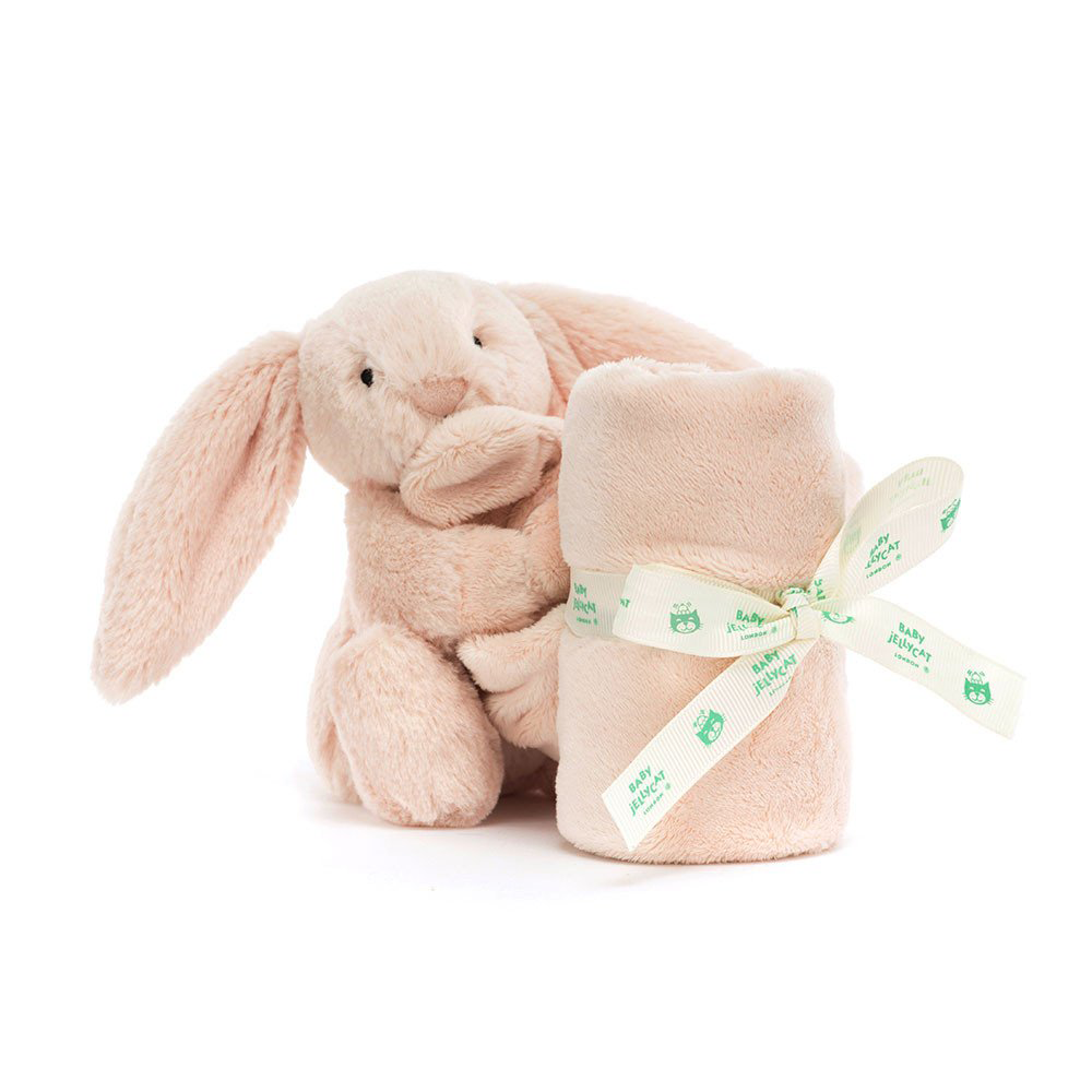 A soft pink plush bunny toy with long ears, holding a pink rolled-up blanket or towel tied with a green and white ribbon that reads 'Baby Jellycat'.