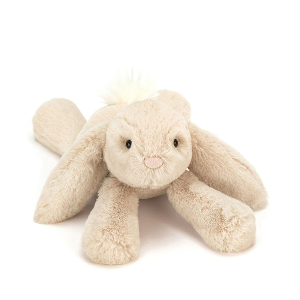 Soft plush toy in the shape of a beige bunny with long ears, black eyes, and a pink nose, lying on a white background.