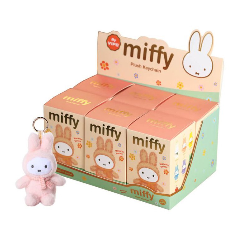 Pink plush keychain featuring Miffy, a white bunny, wearing a pink scarf, hanging on a keyring. Displayed in front of a colorful Miffy plush keychain display box with multiple boxes of Miffy plush keychains on top.