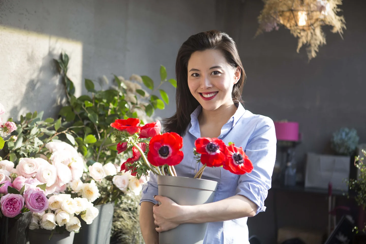 Smiling woman with long black hair holding potted red flowers