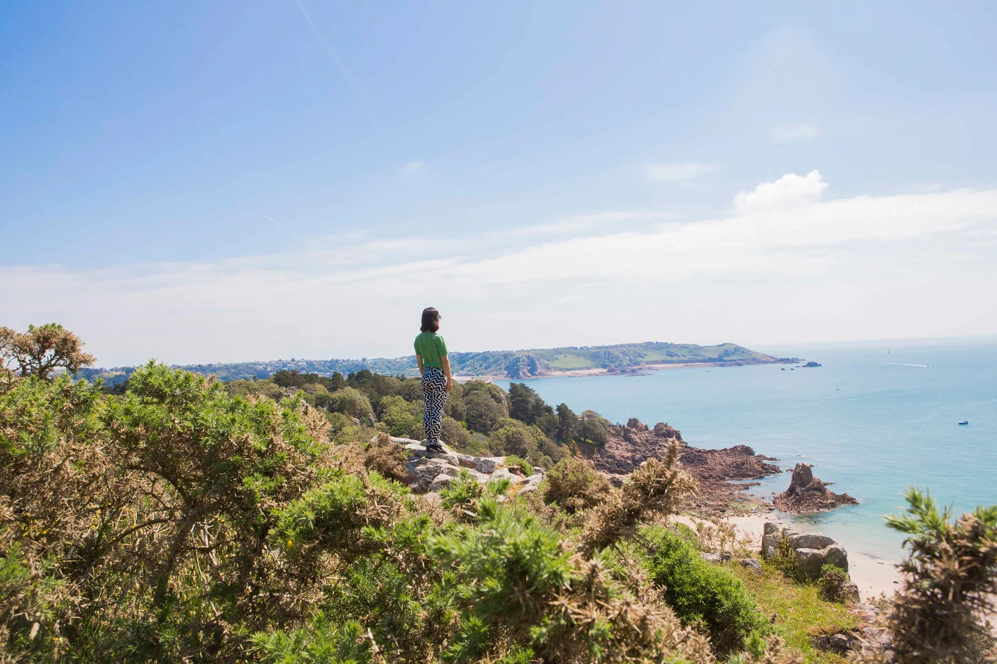 Woman standing alone on grassy knoll gazing out towards the bay