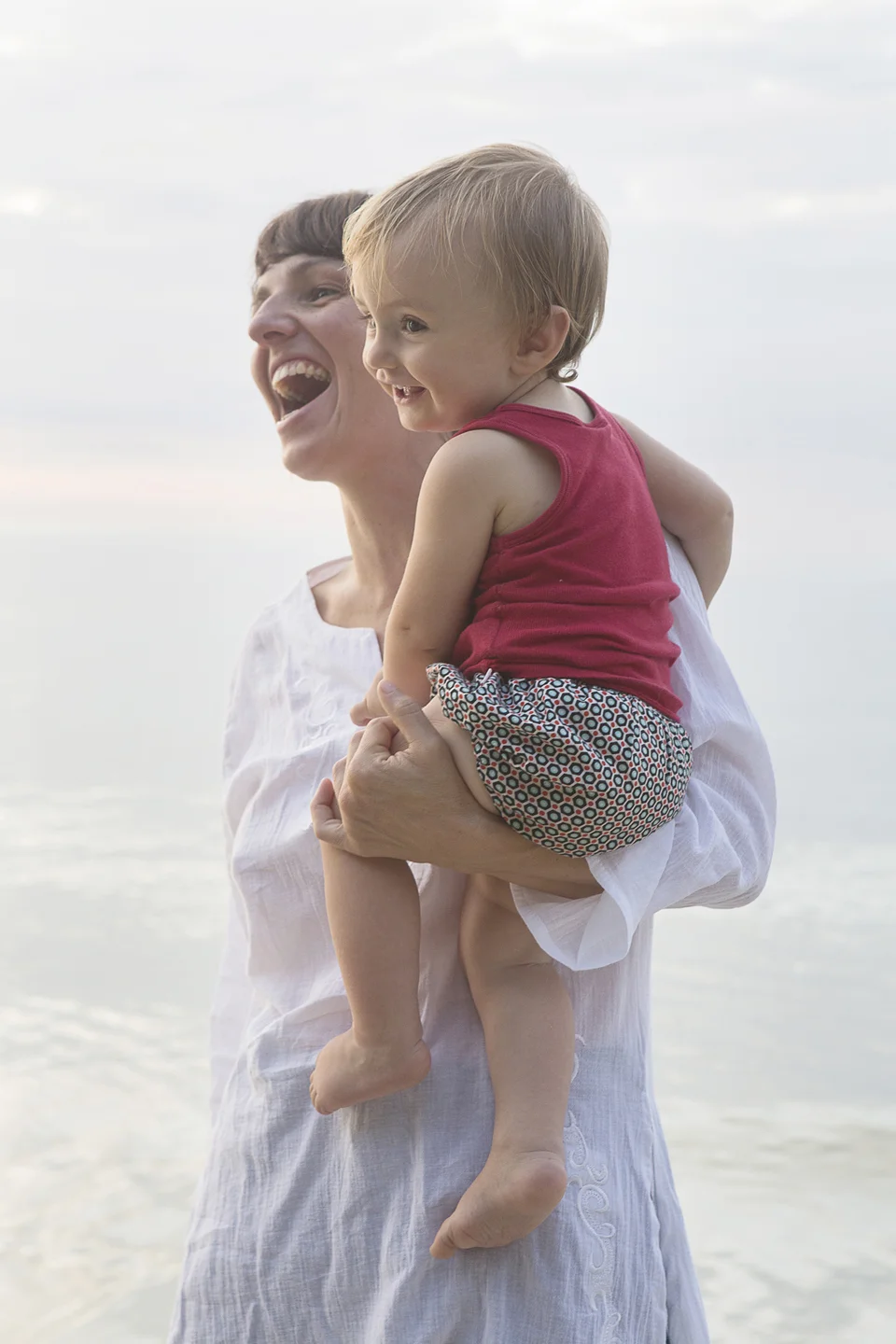 Woman dressed in white laughing and holding child in arms