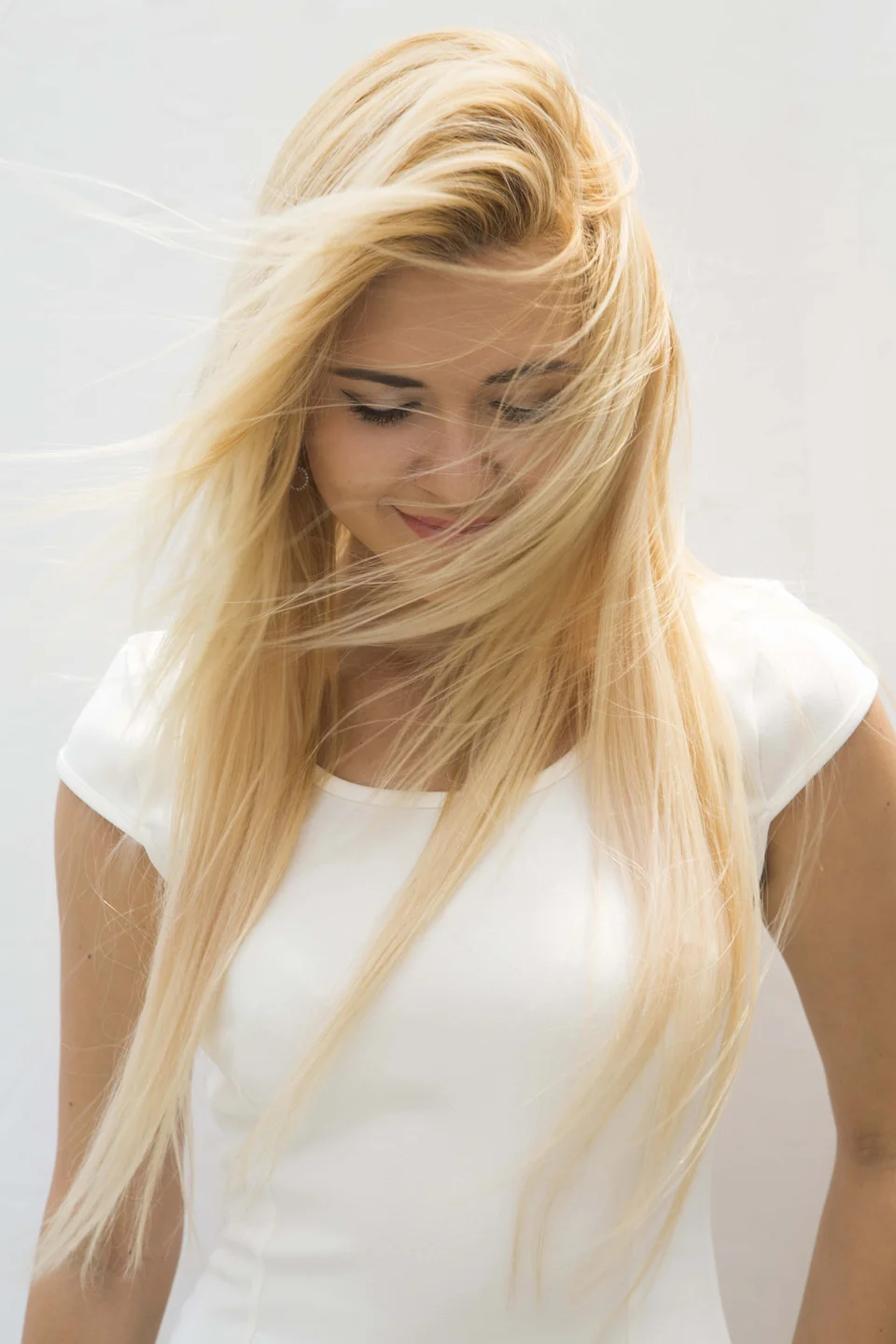 blonde woman with wind-swept hair looking down and smiling