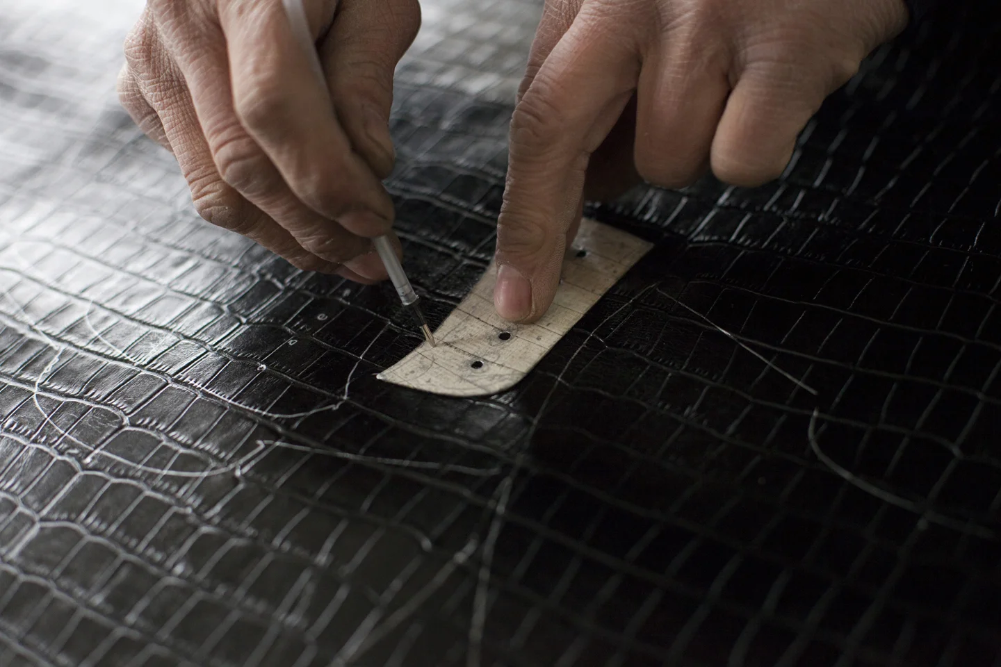 Shoemaker preparing lace holes from leather