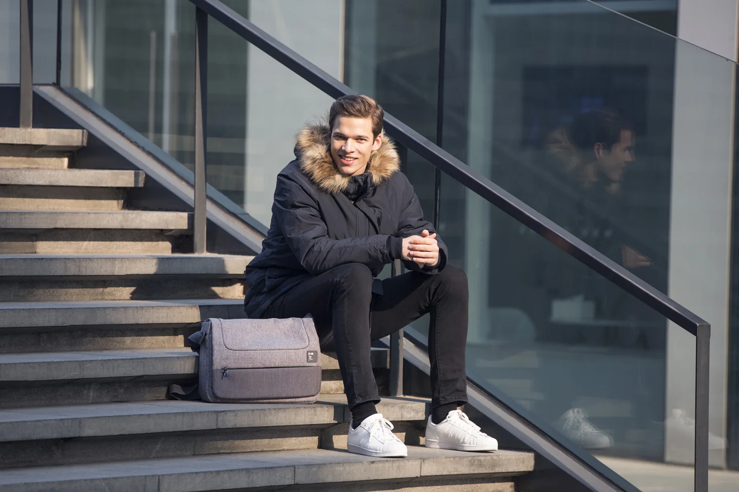 man sitting on stair outside with should strap bag