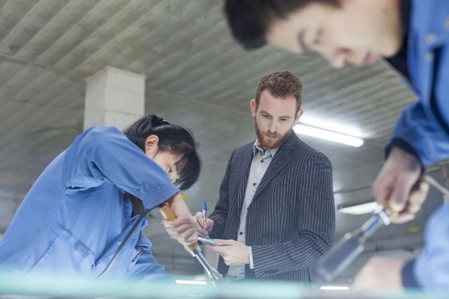 Man holding paper and pen inspecting factory workers