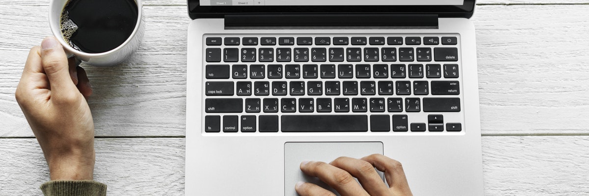Man holding a cup of coffee and looking at a computer