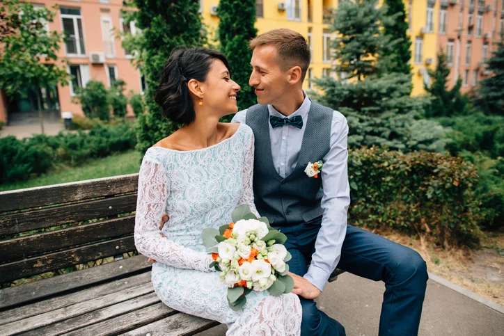 Happy-bride-and-groom-sitting-on-bench-on-wedding-day-912584418_726x484.jpeg