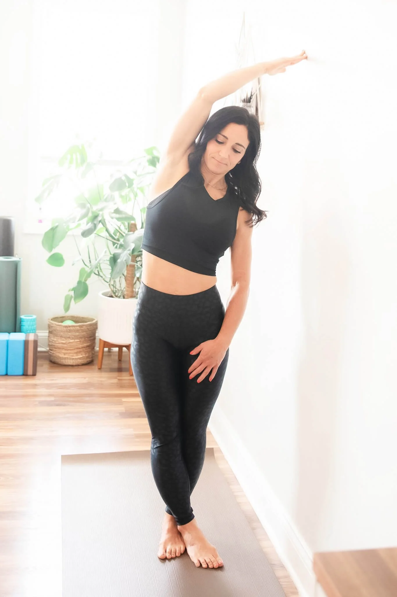 Standing side stretch for upper back and rib cage mobility demonstrated against a wall.