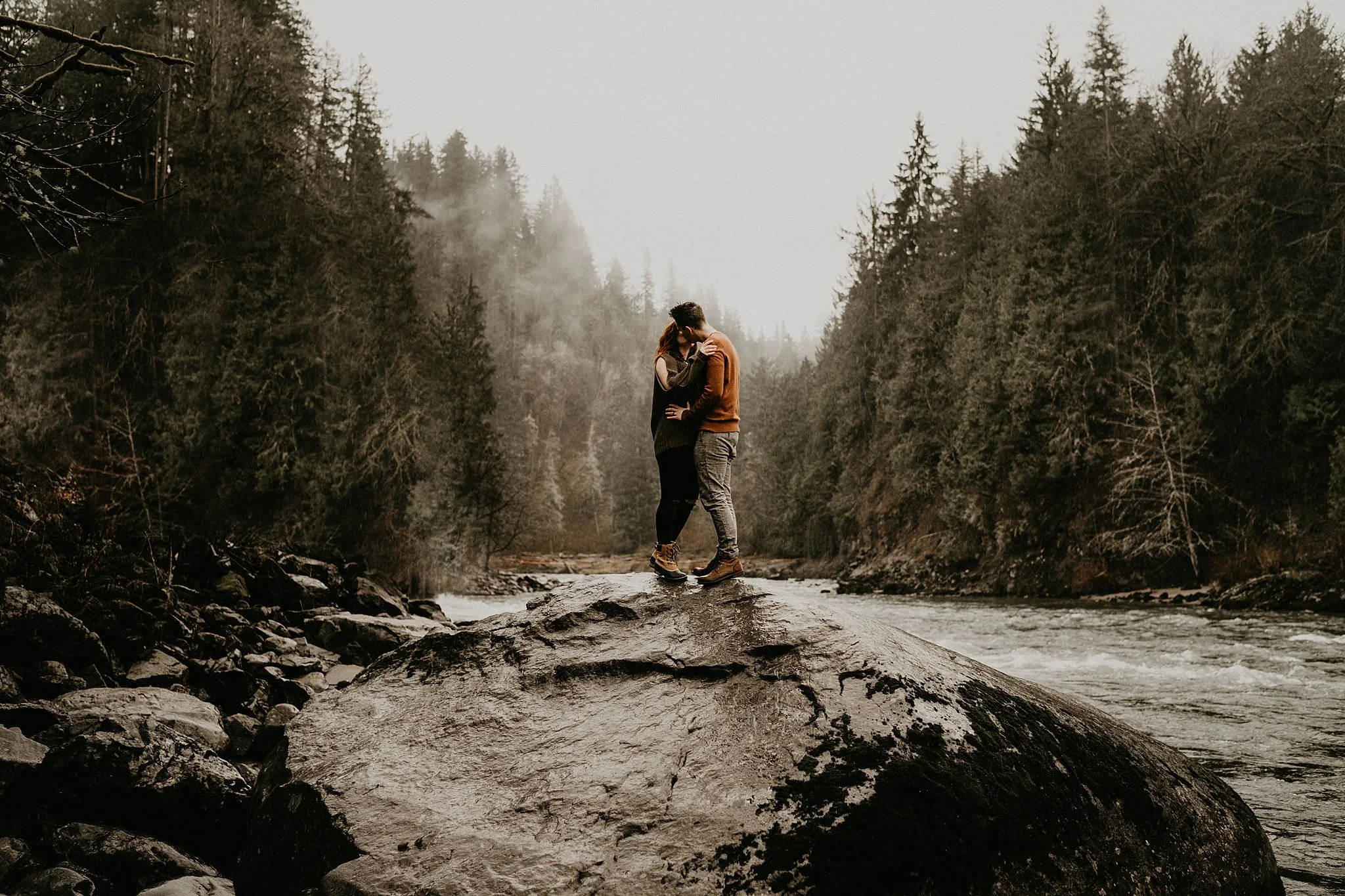 Engagement photo of couple kissing in the rain PNW weather by Snoqualmie Falls Seattle Washington