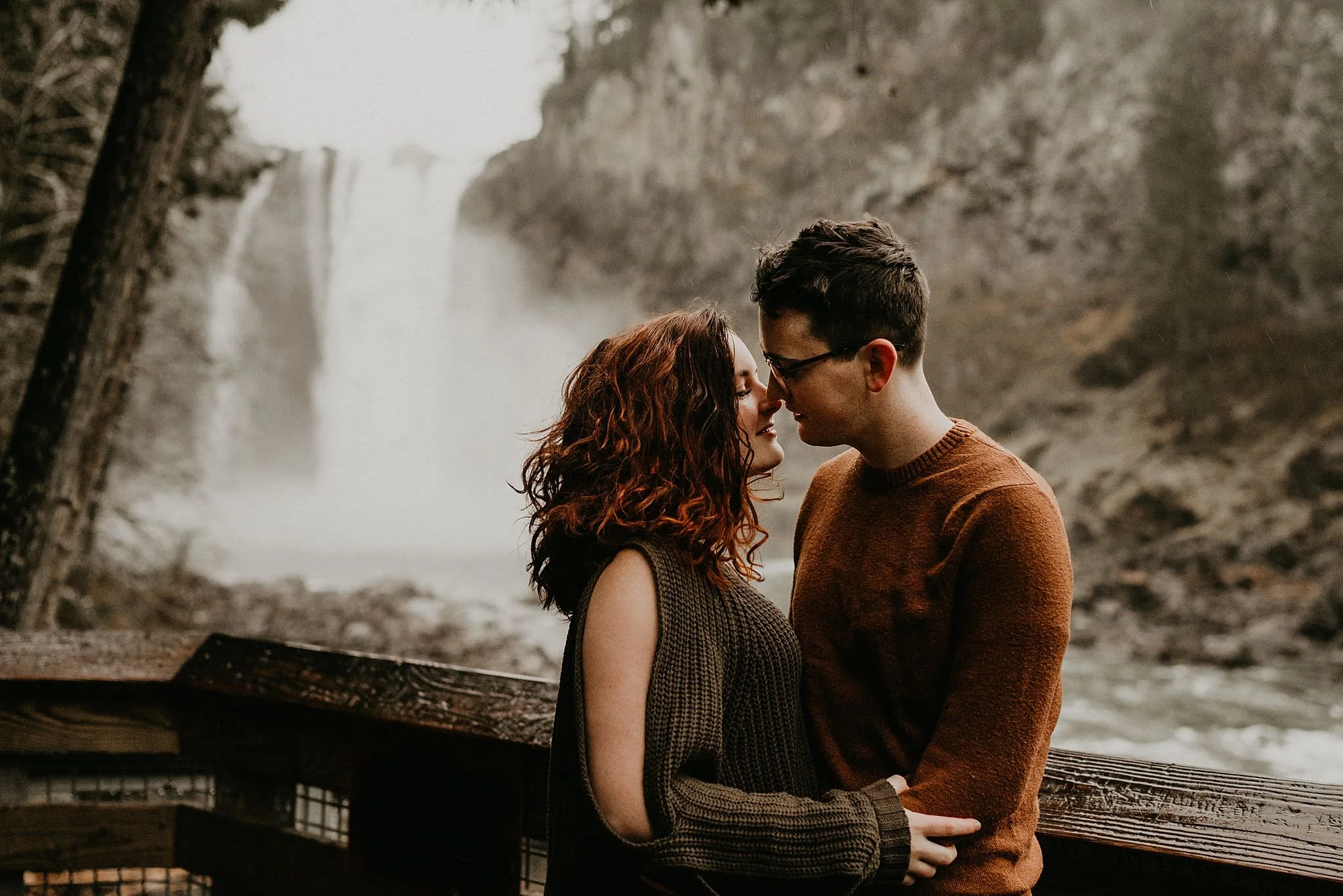 Engaged couple kissing in front of snoqualmie falls