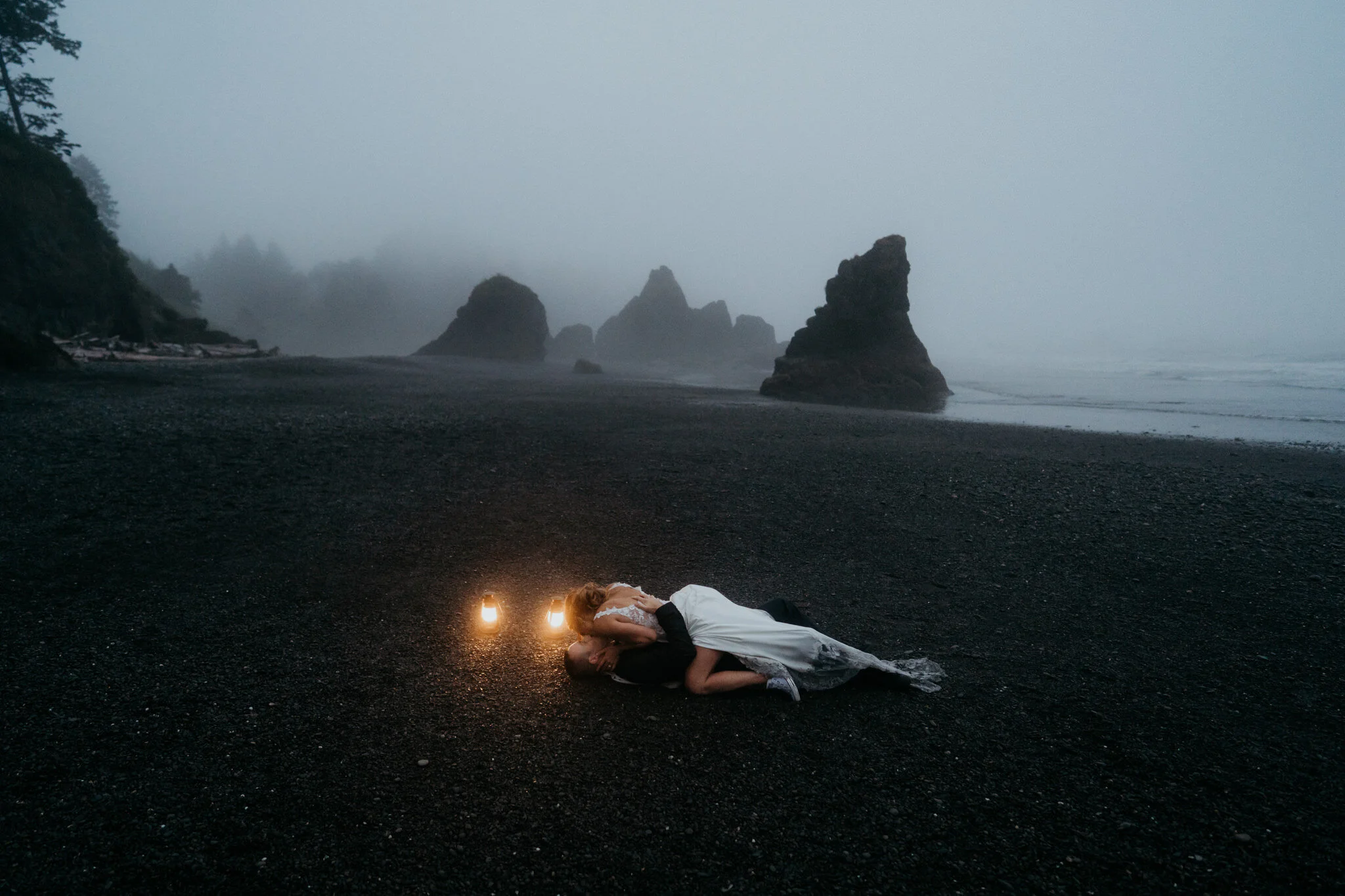 Bride and groom lay on a black sand beach during their elopement at Ruby Beach.