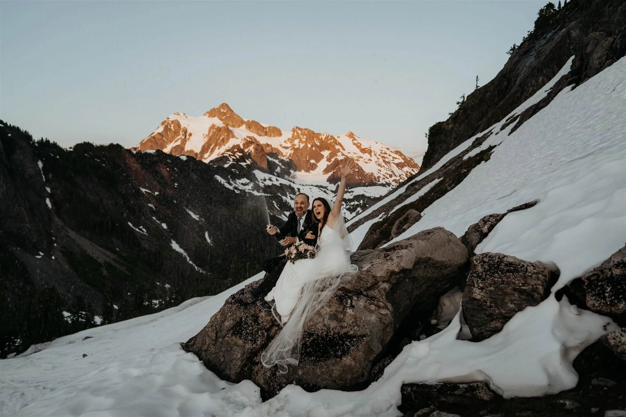 Couple pops a bottle of champagne in the snowy mountains during their elopement in Washington.