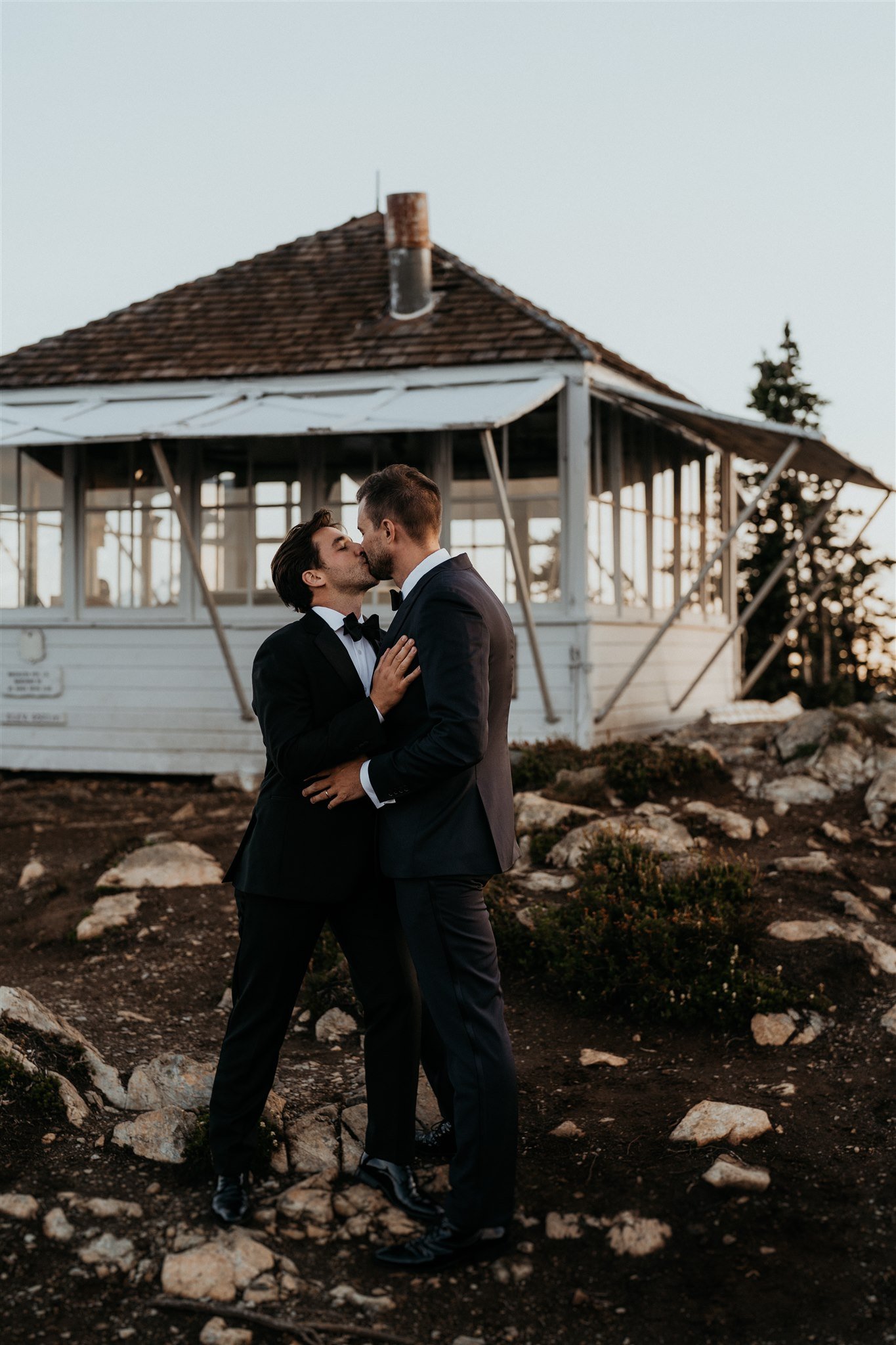 Two grooms kissing in front of a fire lookout in the North Cascades mountains