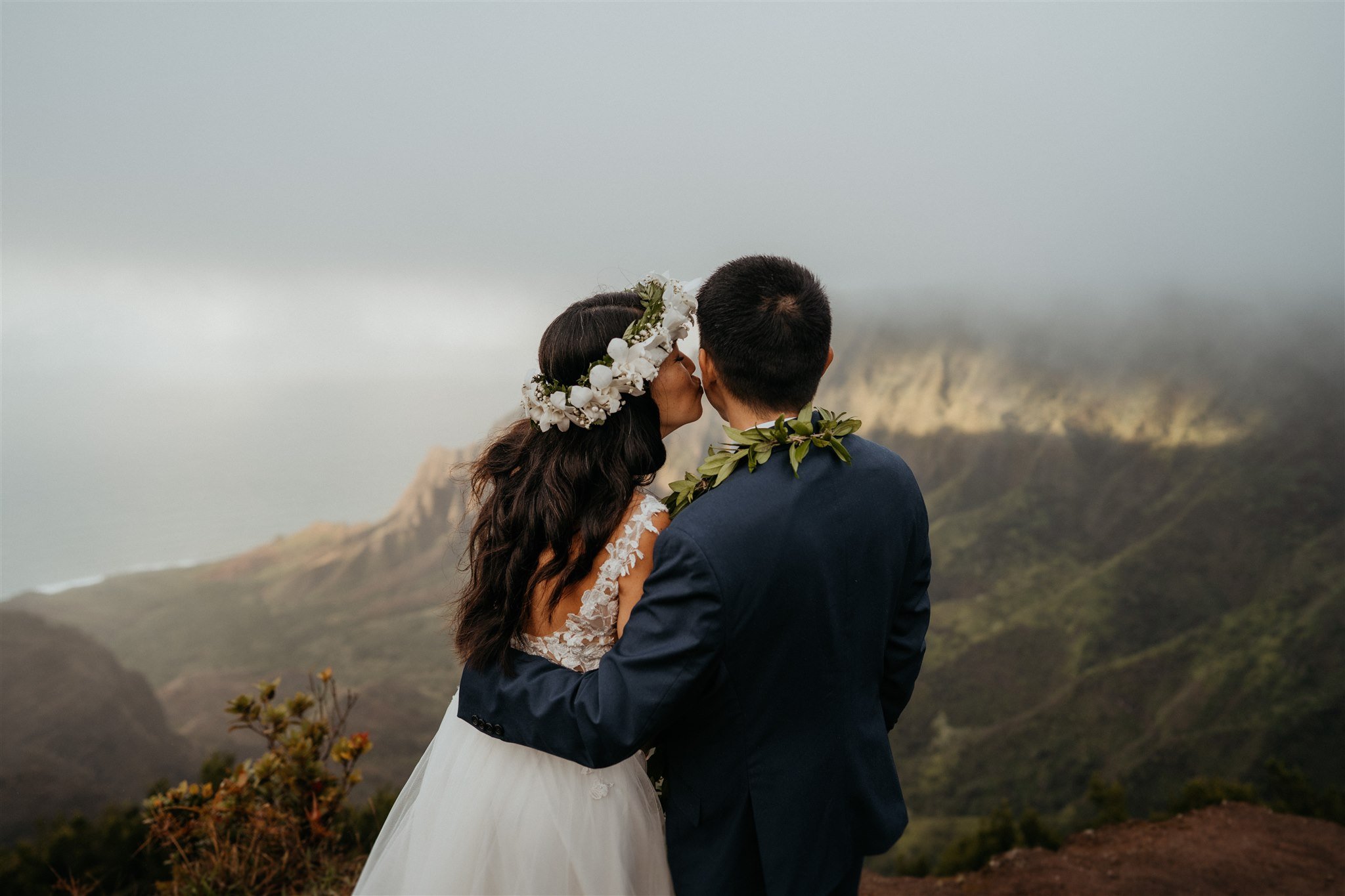 Bride kissing groom at mountain overlook in Kauai