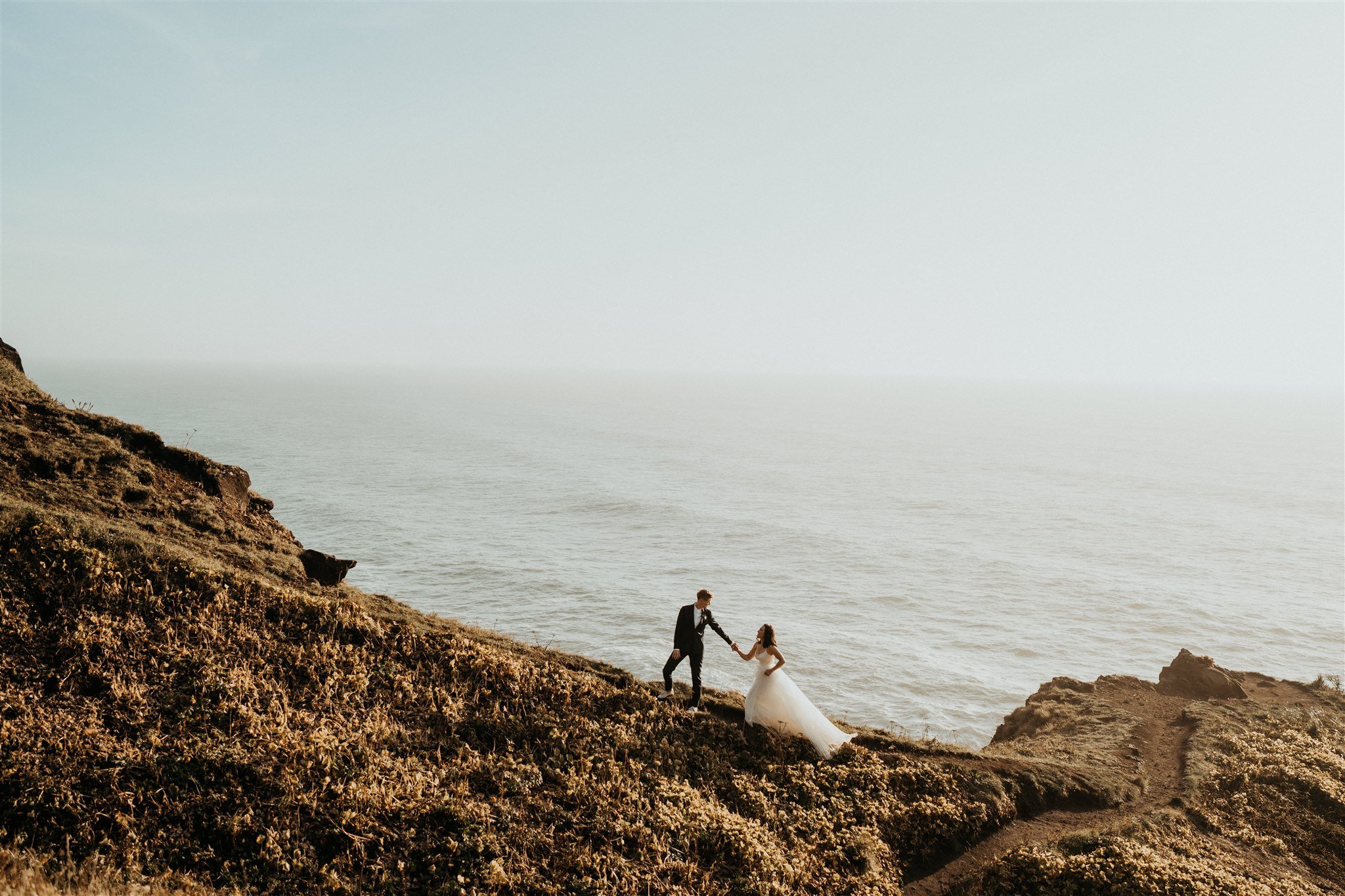 Two brides walking hand in hand for their elopement on the Oregon cliffs