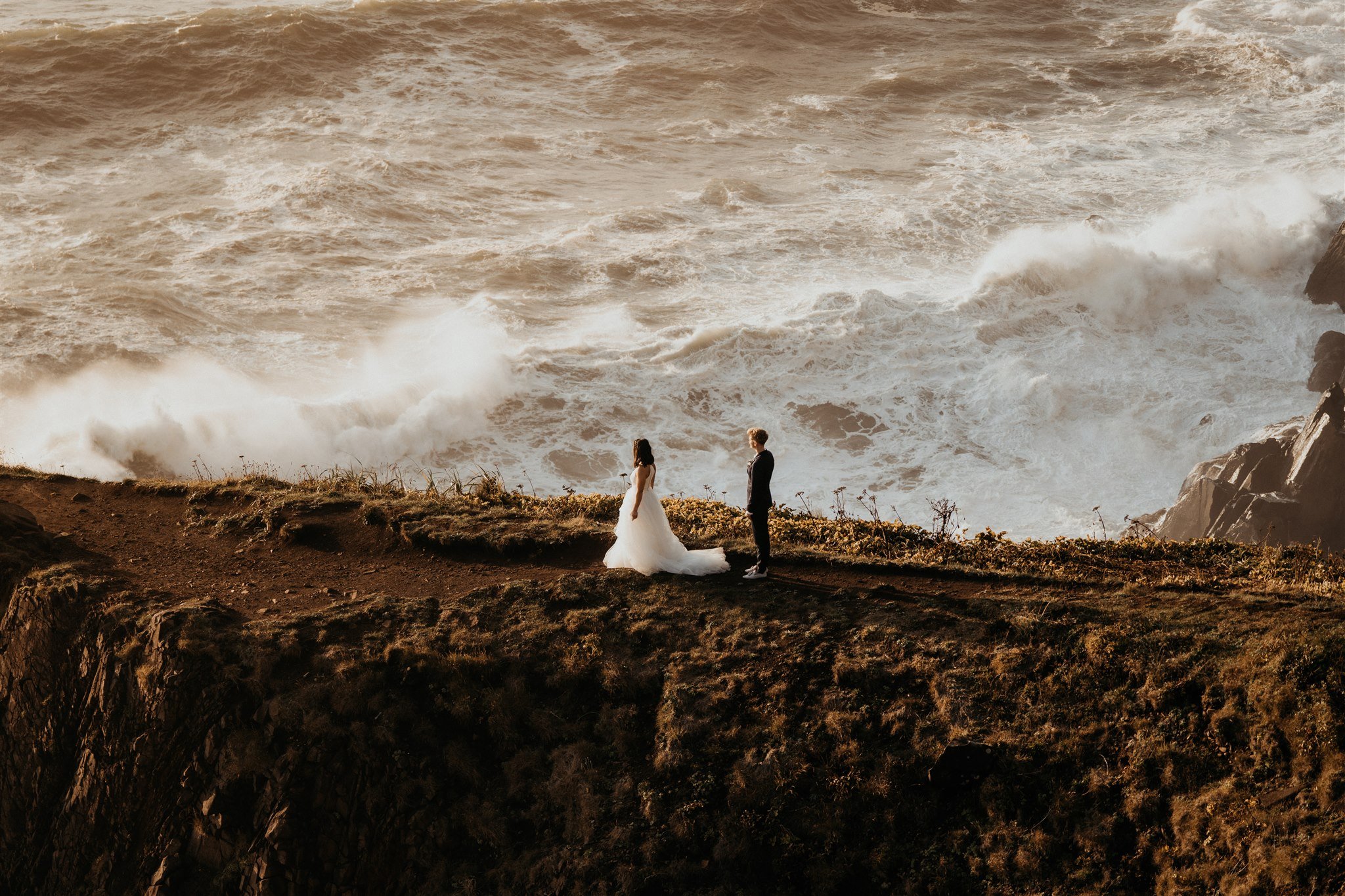 Two brides walking along the Oregon cliffs at sunset for their elopement