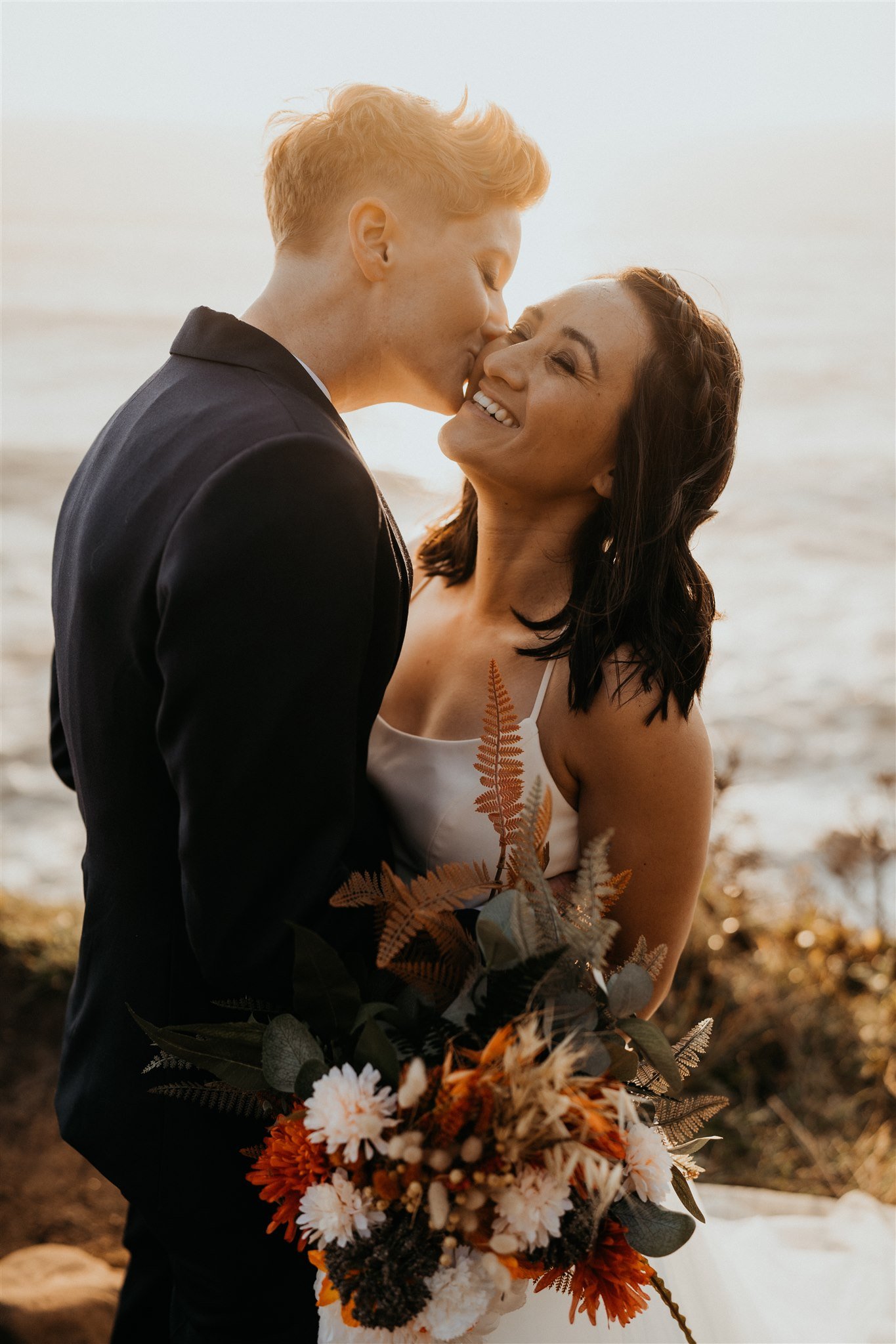 Two brides kiss during sunset at their Oregon Coast elopement