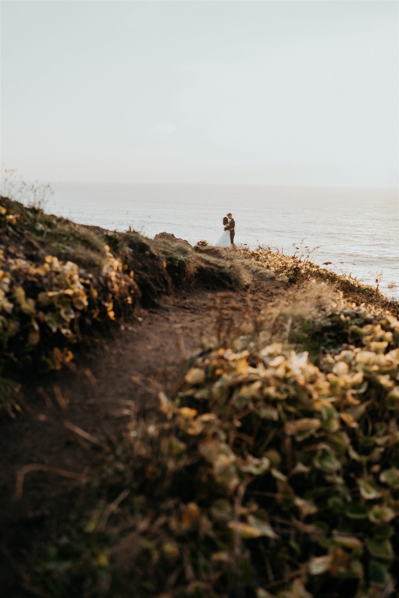 Two brides standing on the Oregon cliffs at their elopement