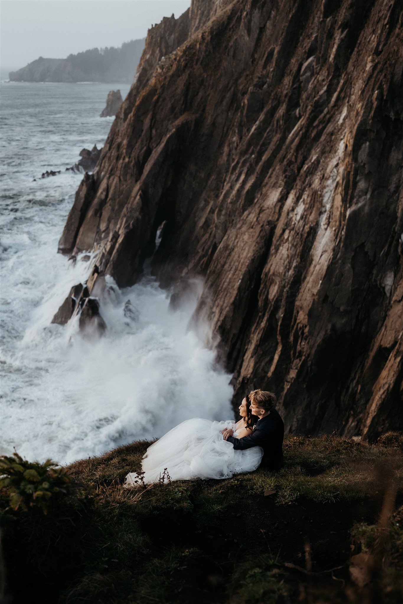 Two brides sitting on the cliff watching the waves for their Oregon Coast elopement
