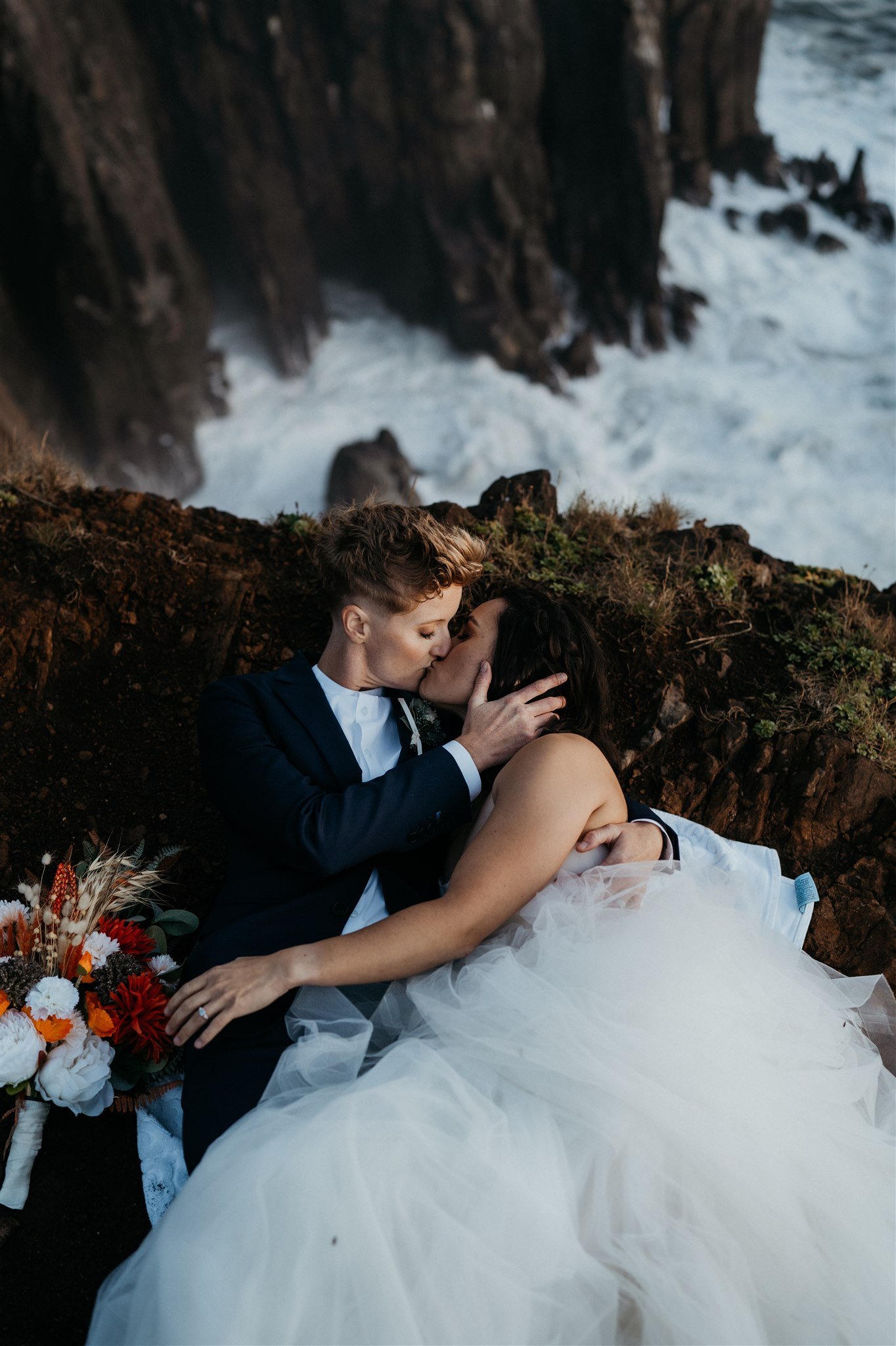 Two brides laying down and kissing on the Oregon Cliffs for their elopement