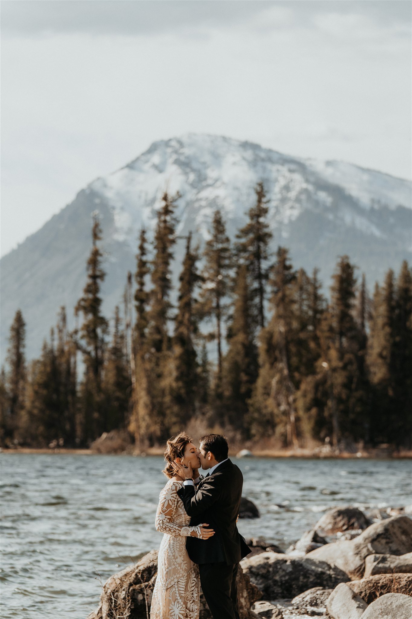 Bride and groom kiss in front of the lake and mountains at Lake Wenatchee