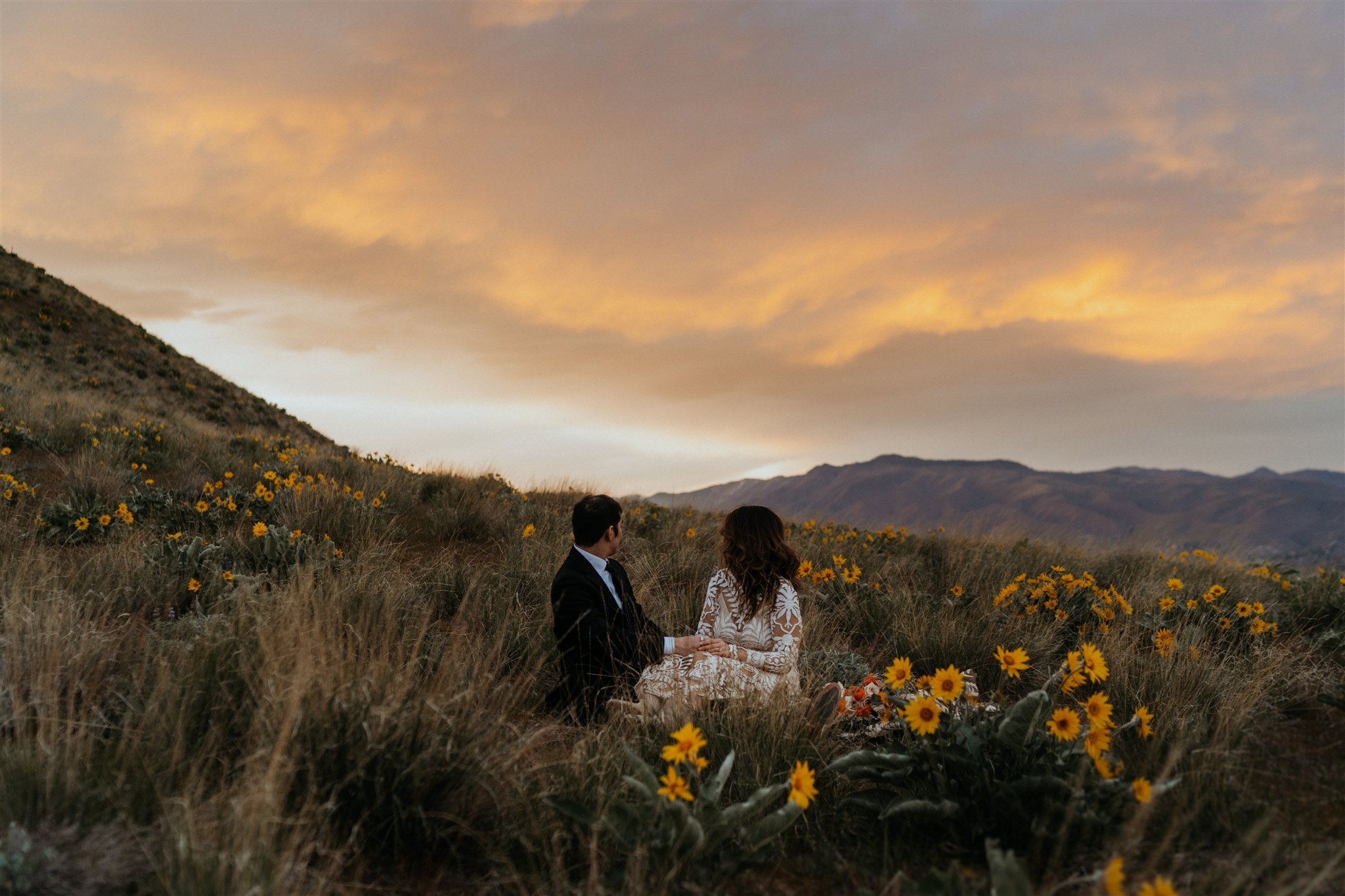 Bride and groom sitting in a wildflower field overlooking the city