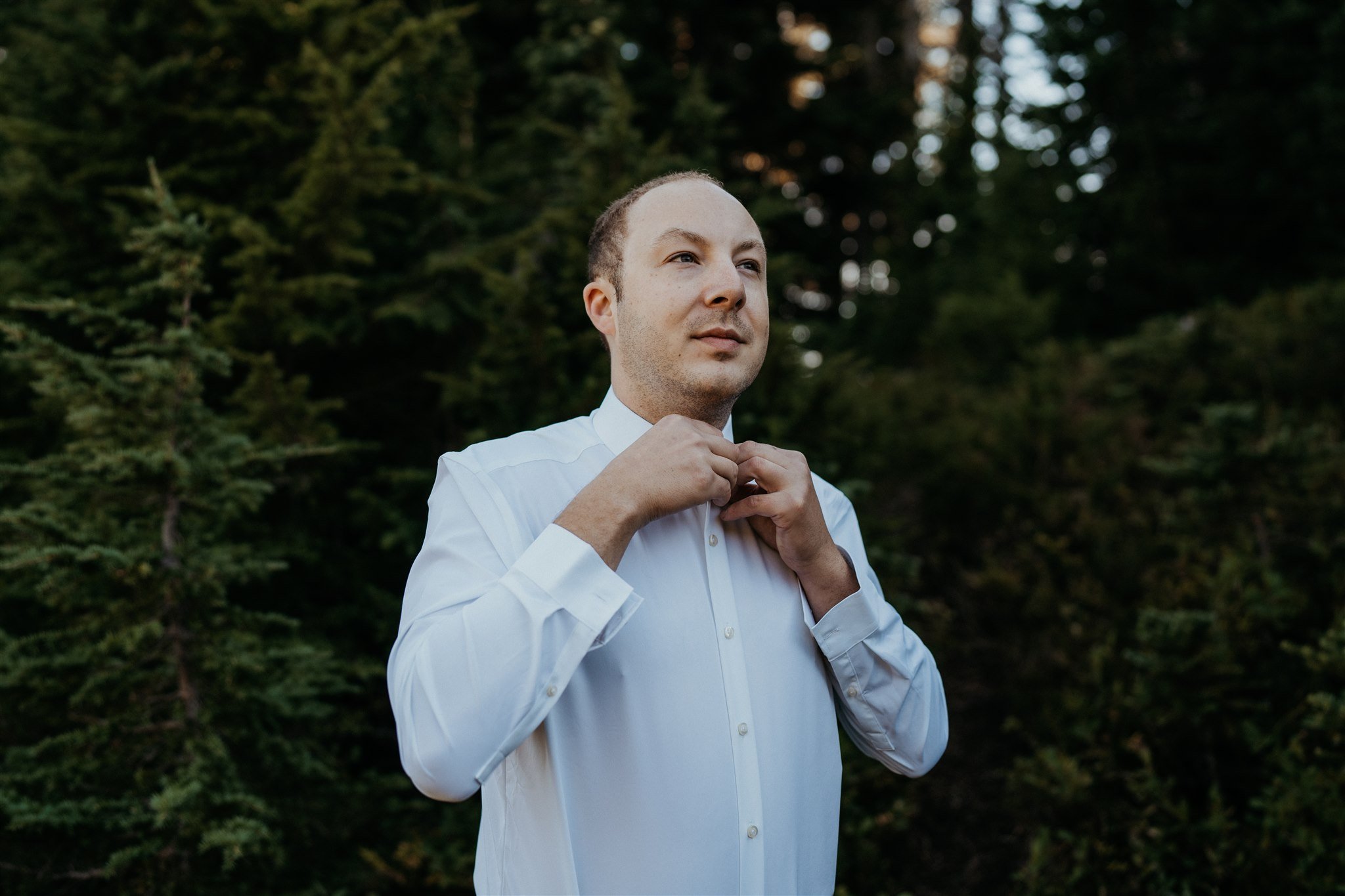 Groom buttoning shirt while getting ready at Mt Rainier National Park