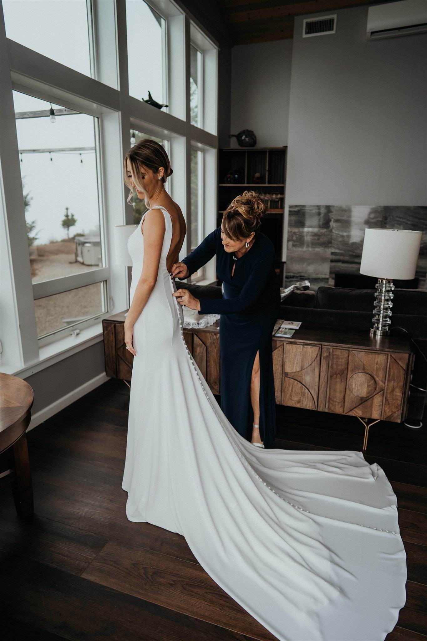 Mother of the Bride zipping white wedding dress while bride is getting ready