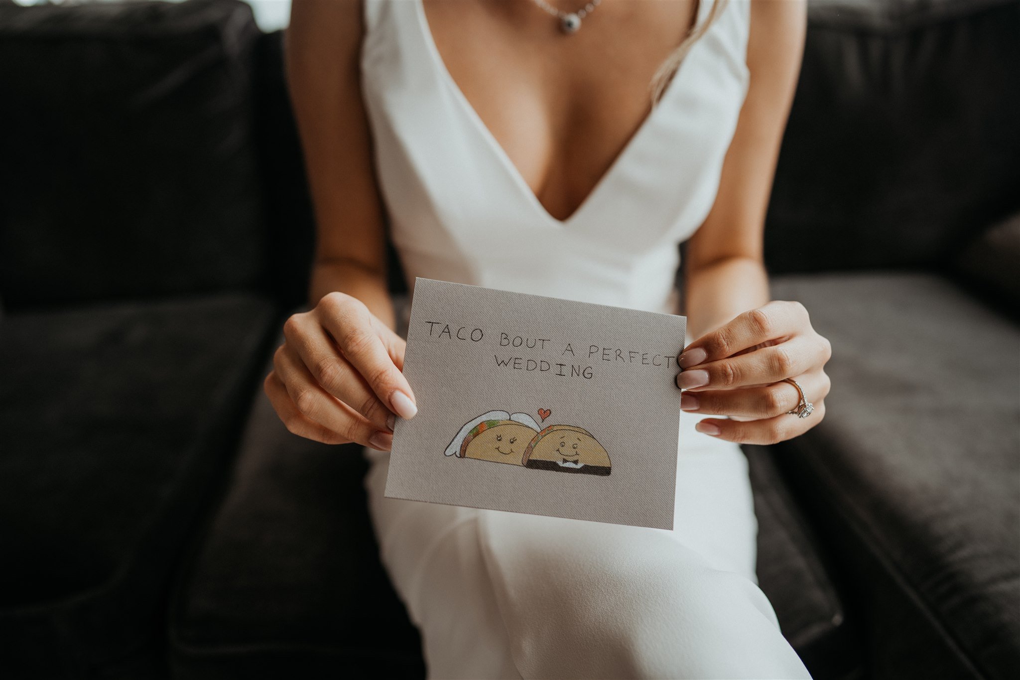 Bride holding handwritten card that reads " Taco Bout a Perfect Wedding"