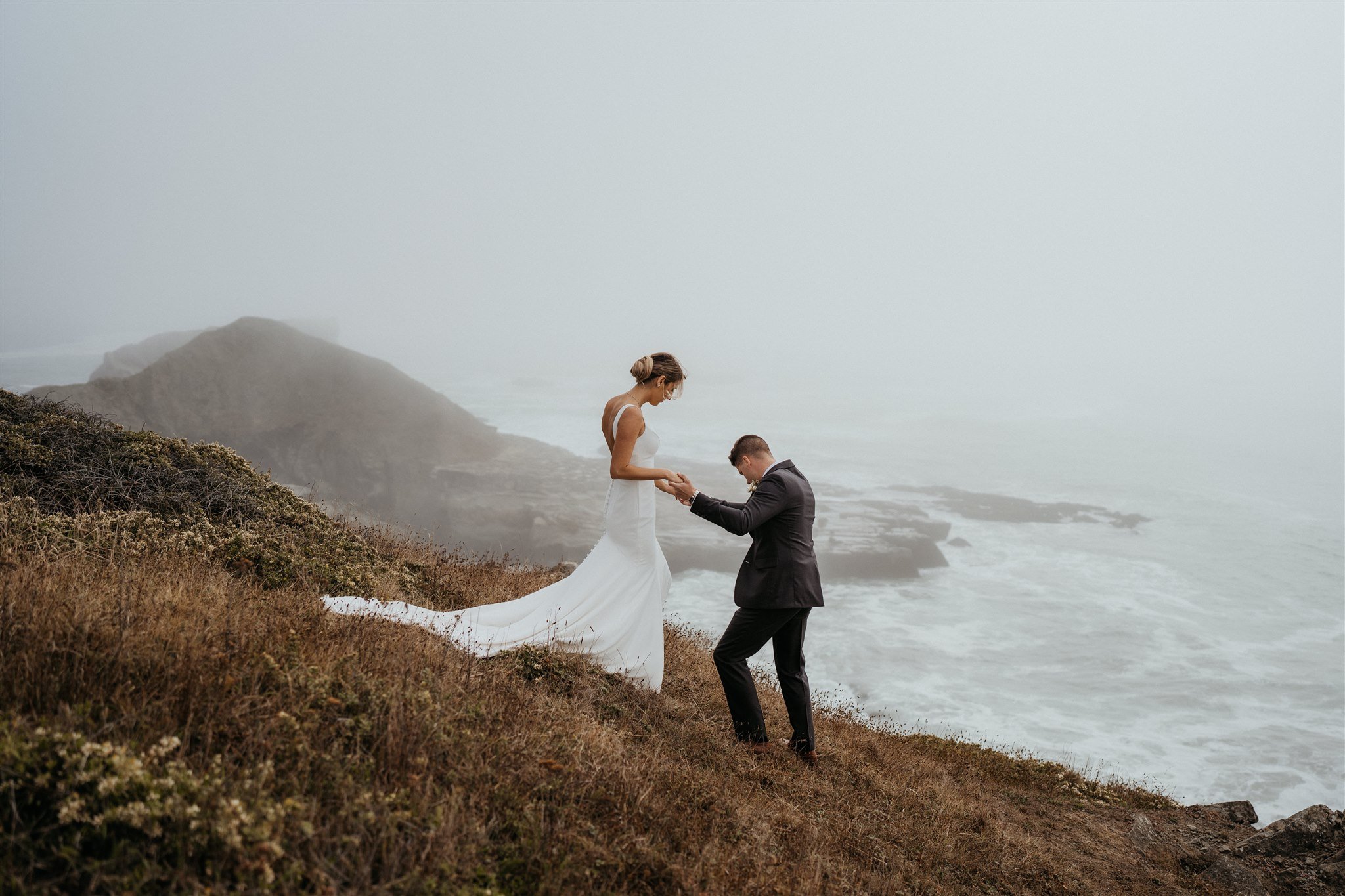 Groom helping bride down the trail to overlook the water on the Southern Oregon Coast