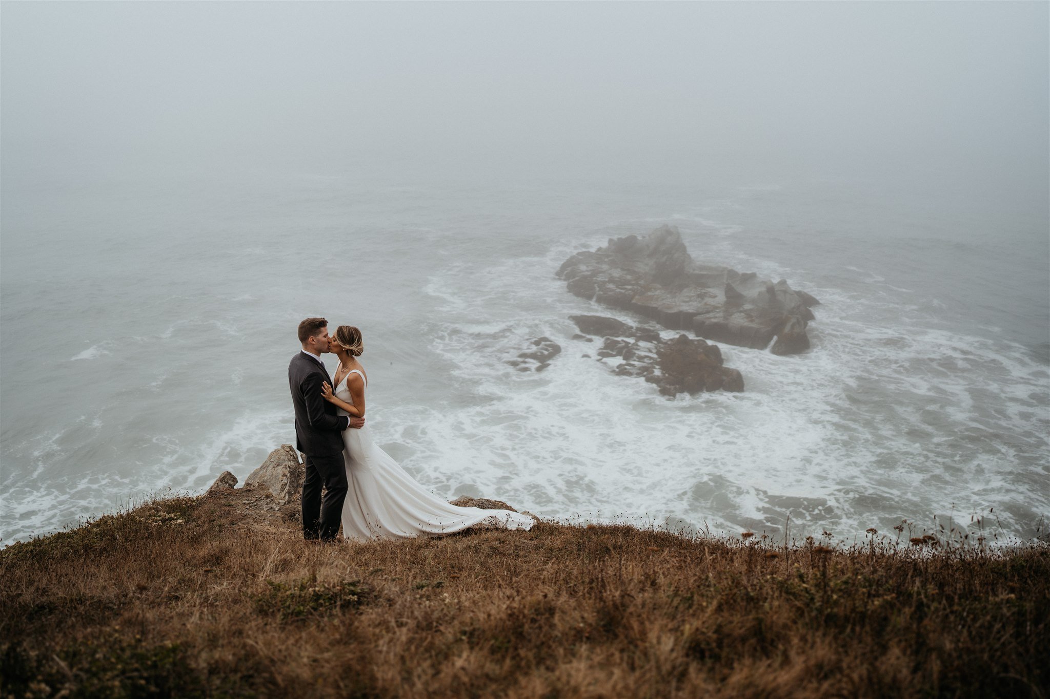 Bride and groom kiss on a cliff overlooking the Southern Oregon Coast
