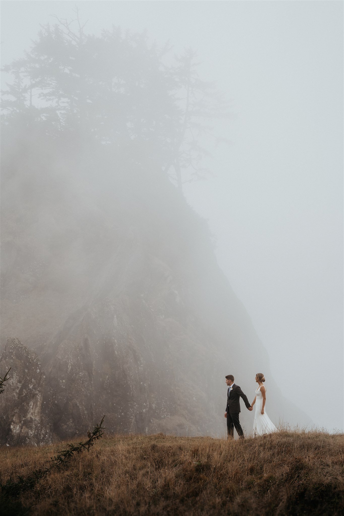 Bride and groom holding hands walking along the trail at the moody Southern Oregon Coast