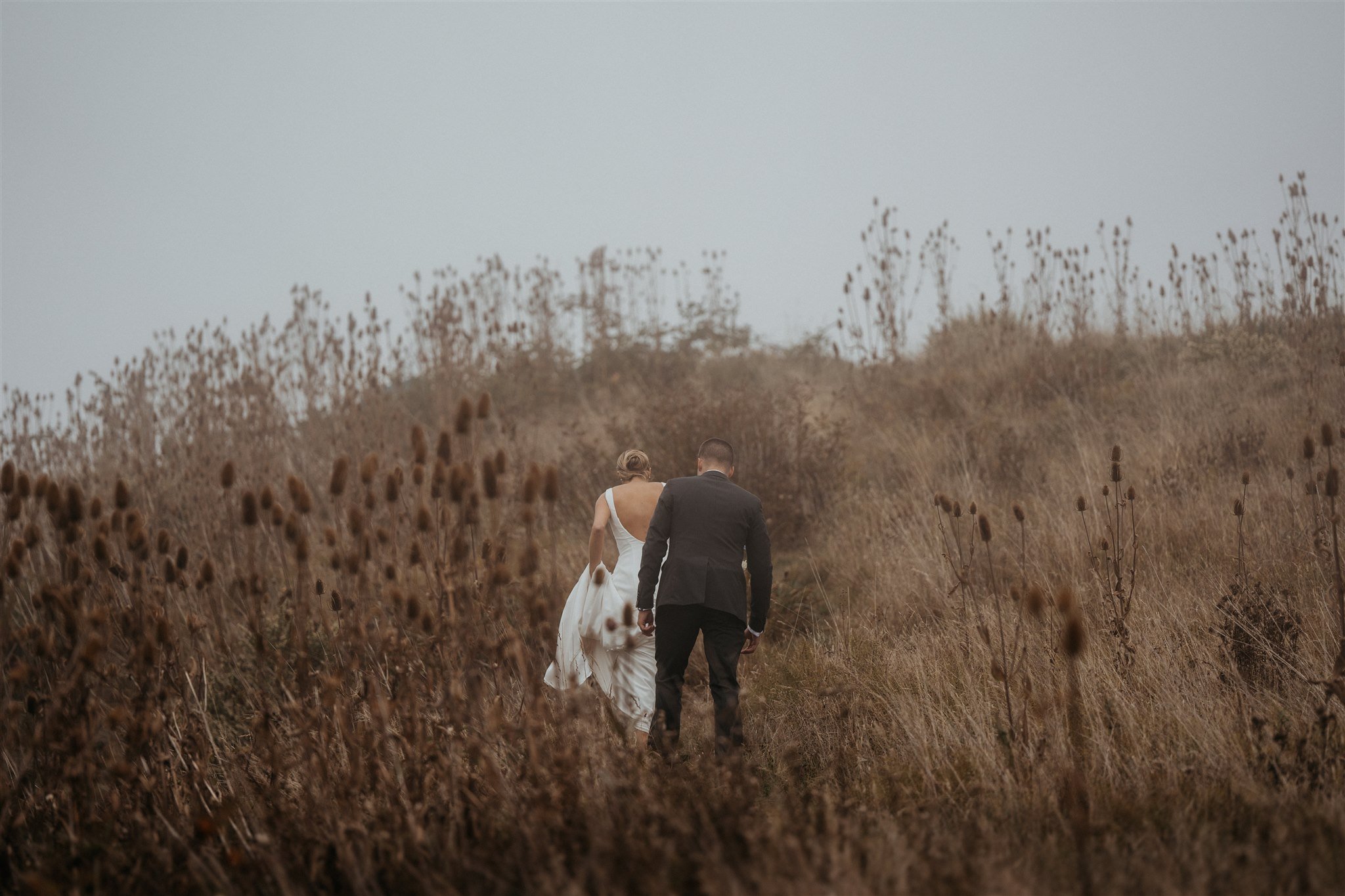 Bride and groom walking through the grass with fog all around
