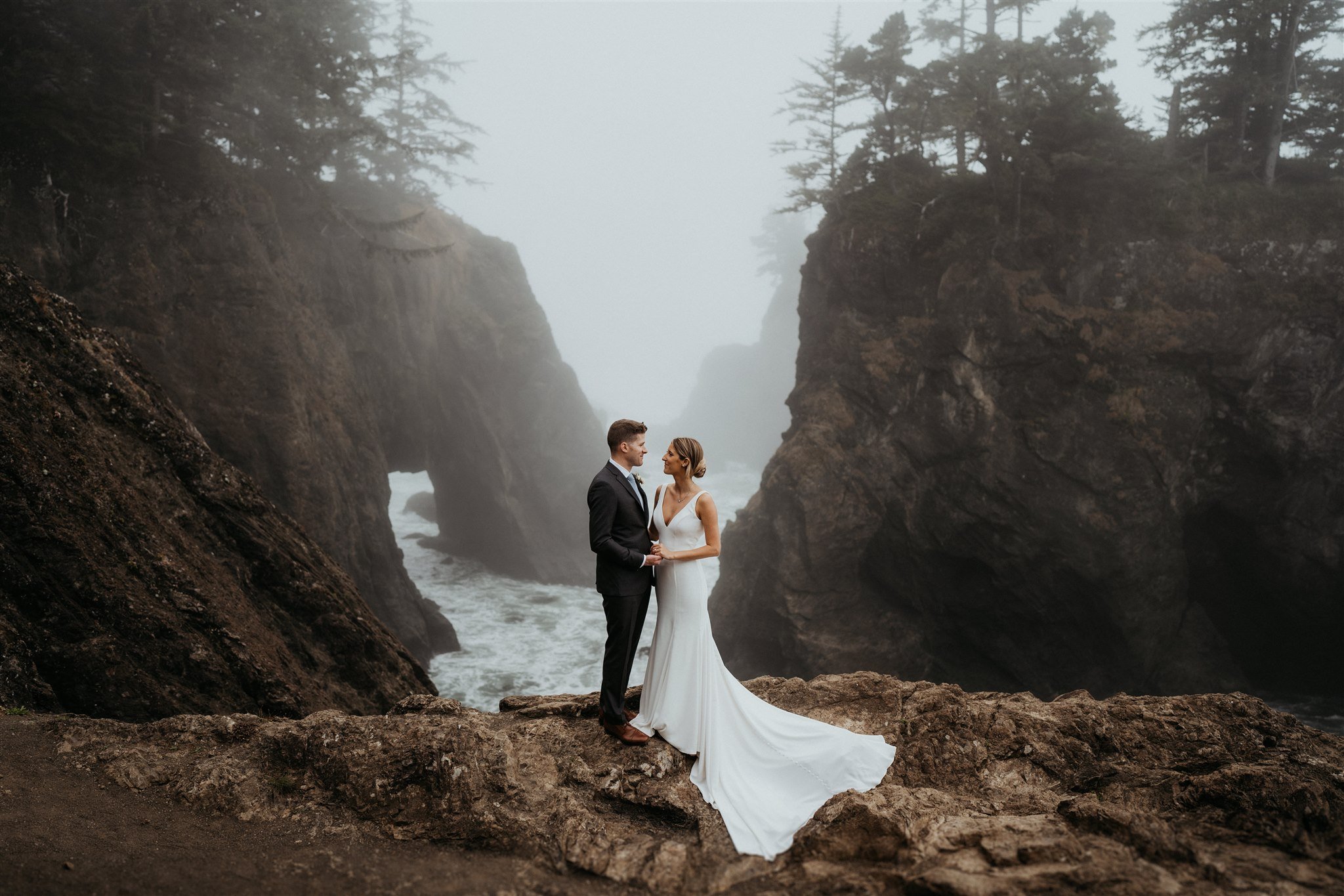 Bride and groom holding hands and standing on the edge of a cliff on the Southern Oregon Coast