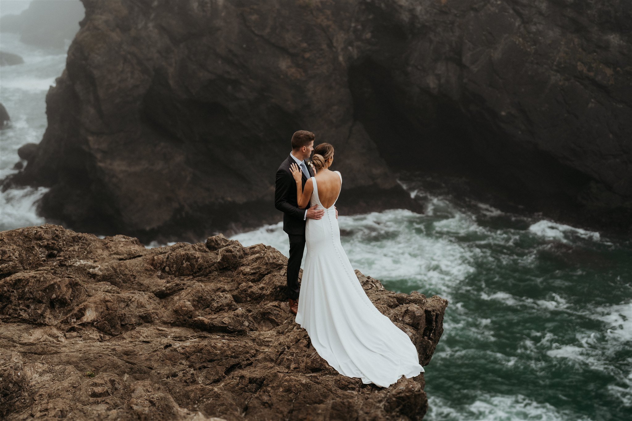 Bride and groom hugging and looking out at the water on the Oregon Coast