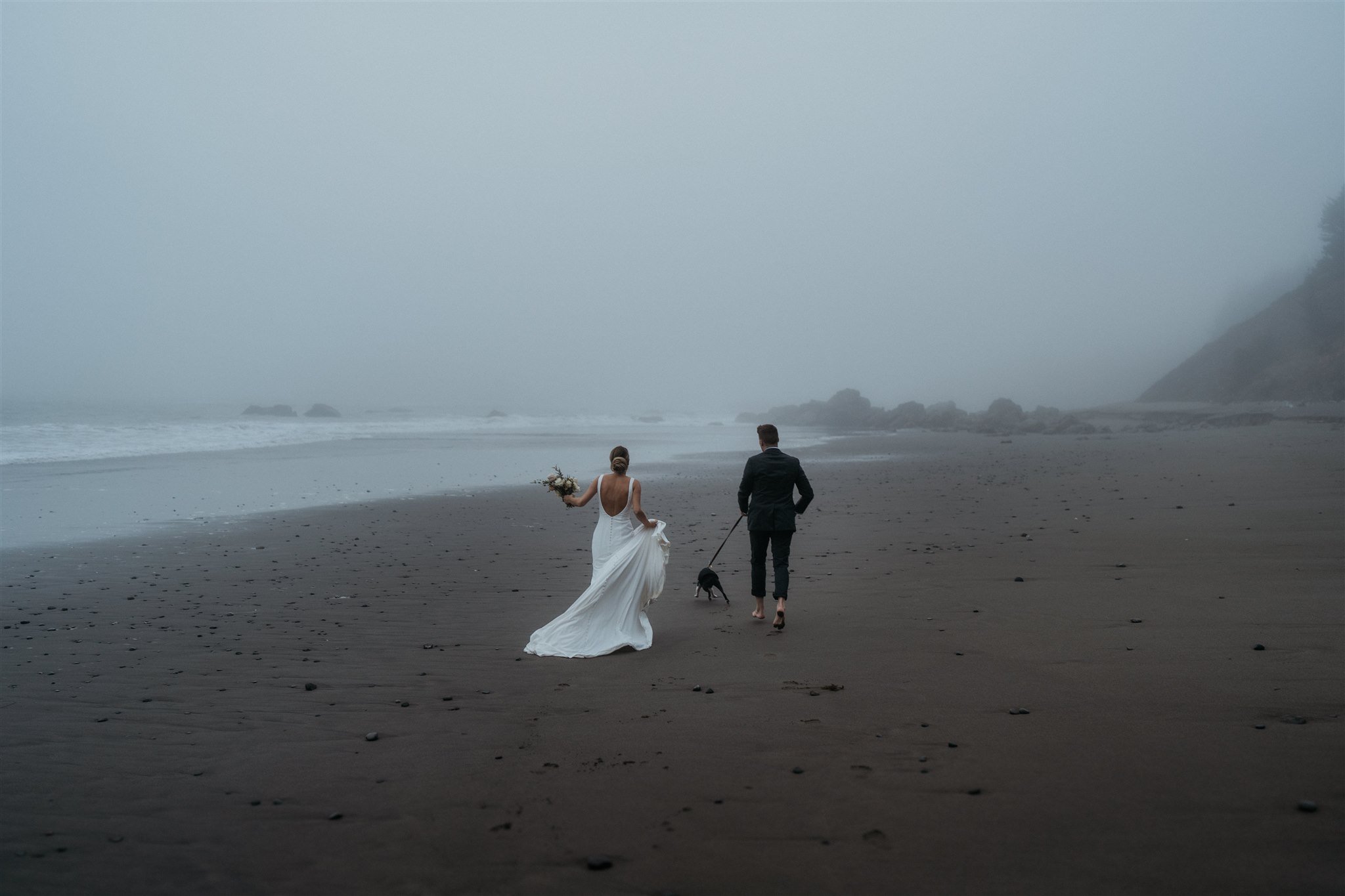 Bride and groom running along the beach with their dog on the Oregon Coast