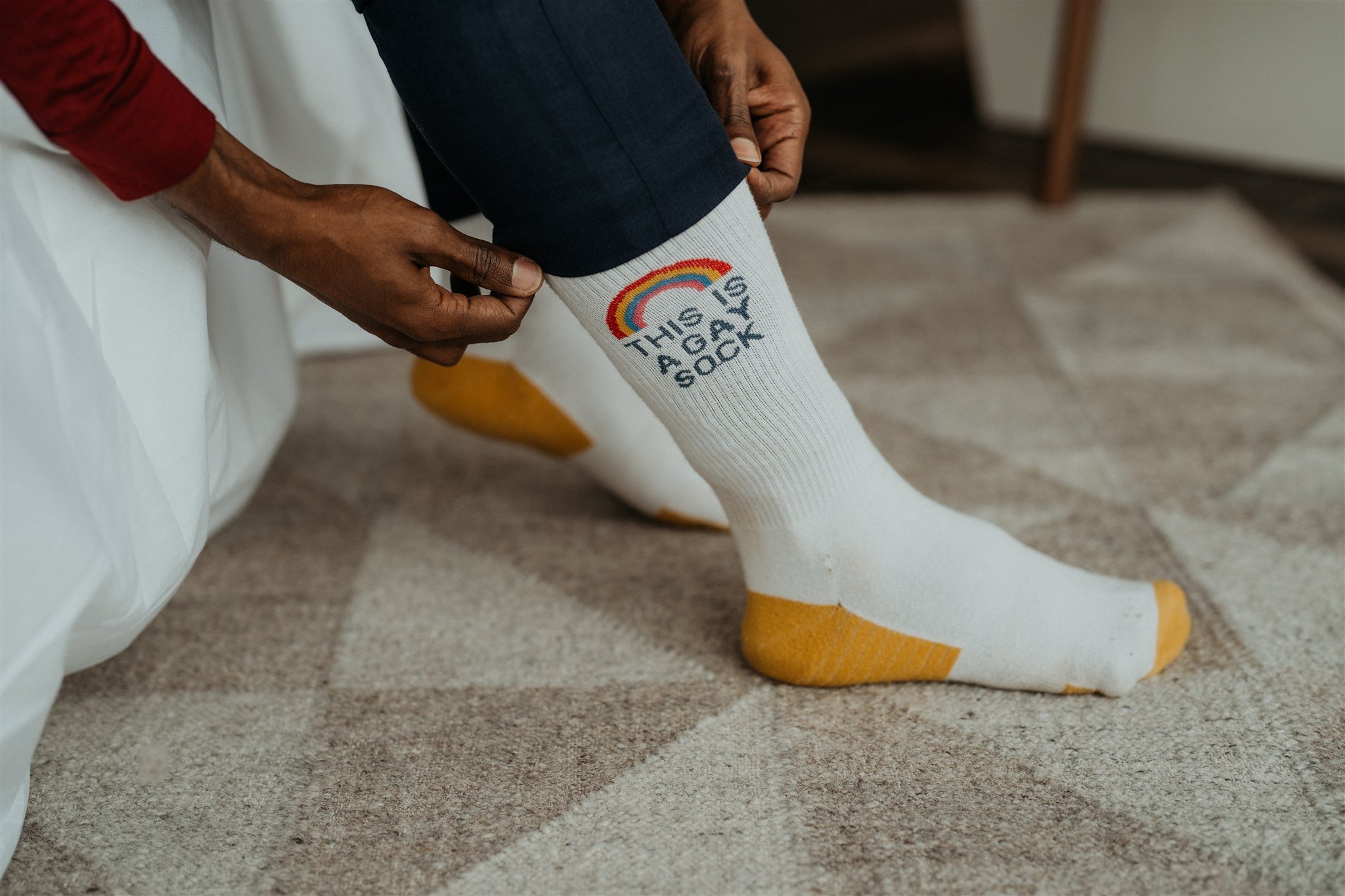 Groom pulling up white and yellow sock that reads "This is a gay sock"