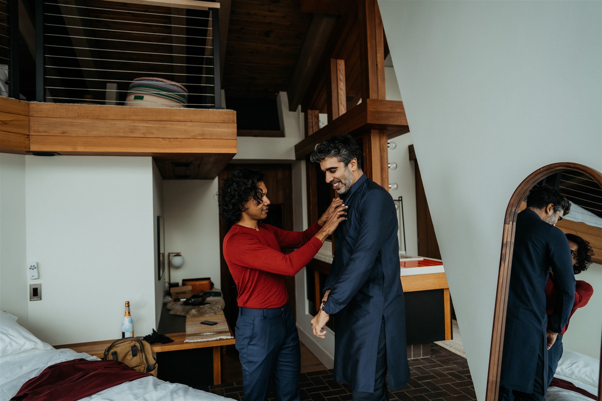 Two grooms helping each other into their wedding outfits for their Colorado winter elopement