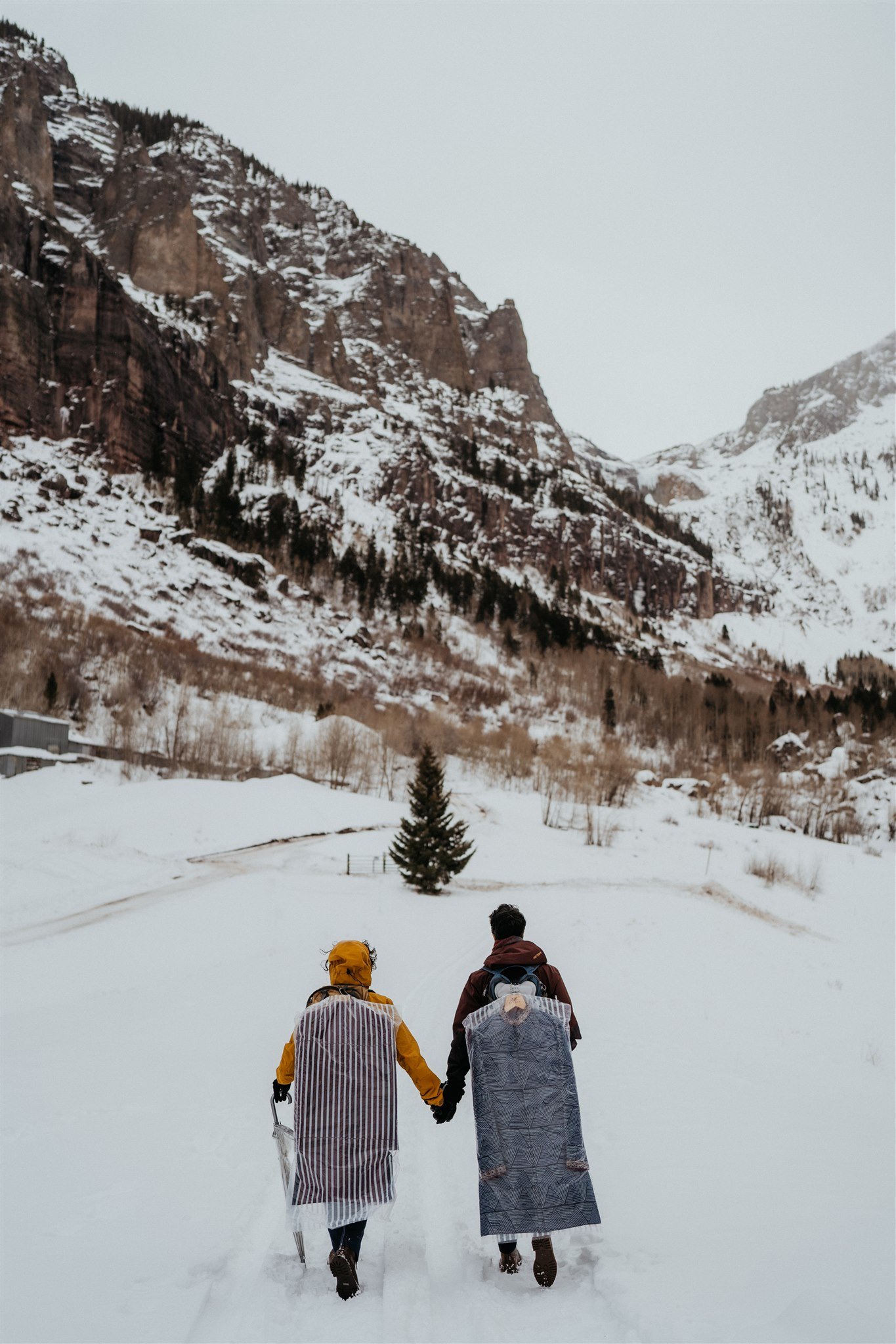 Grooms walking hand in hand up the Colorado mountains for their winter elopement