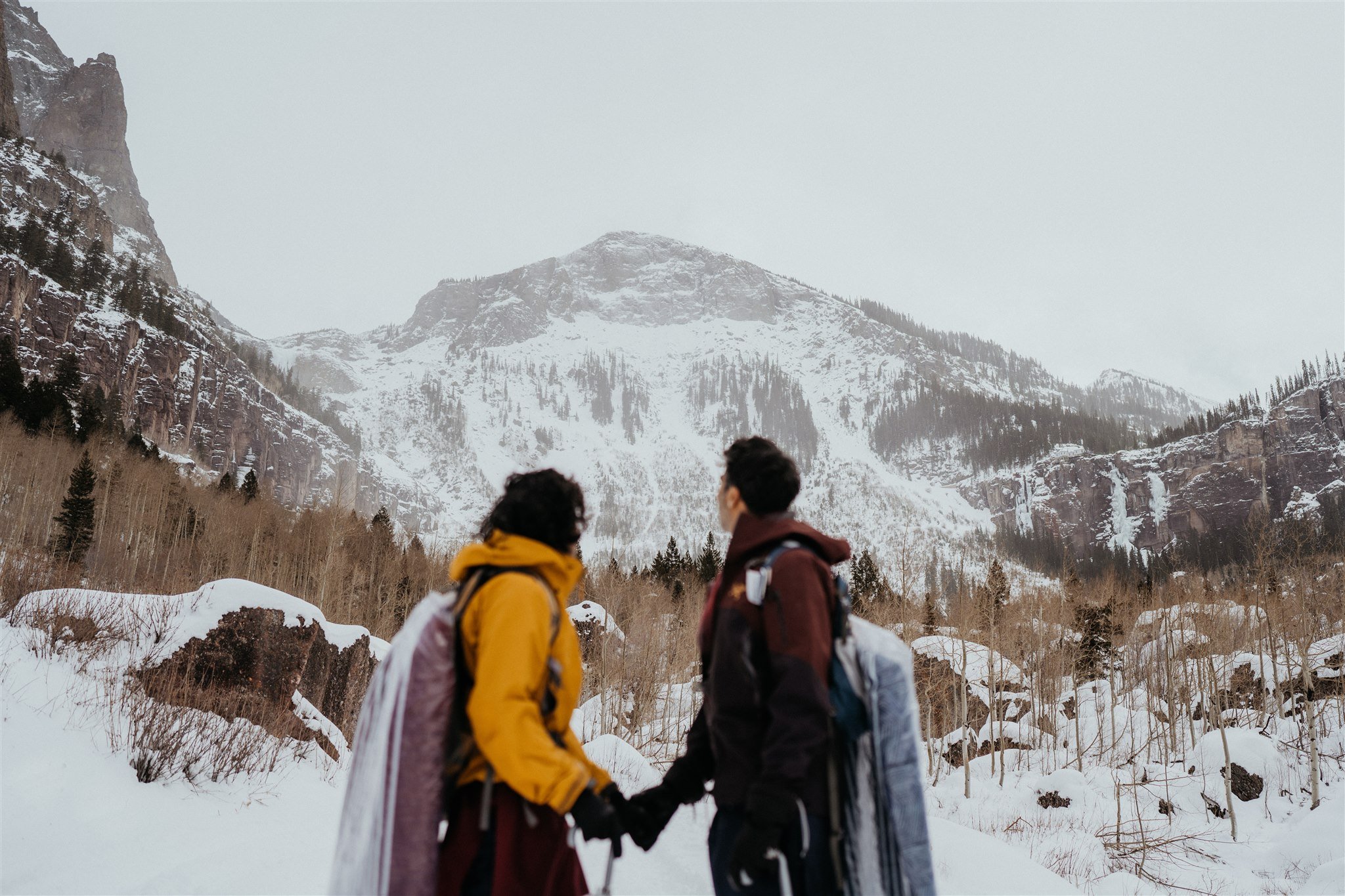 Two grooms holding hands and looking up into the Colorado mountains